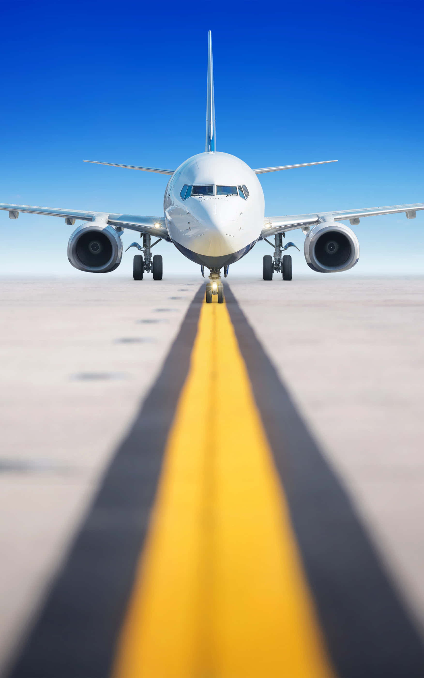 飛機掠過跑道中線 Android 背景 壁紙 — 一架商用飛機在晴朗藍天下，面向跑道上一條醒目的黃色中心線。