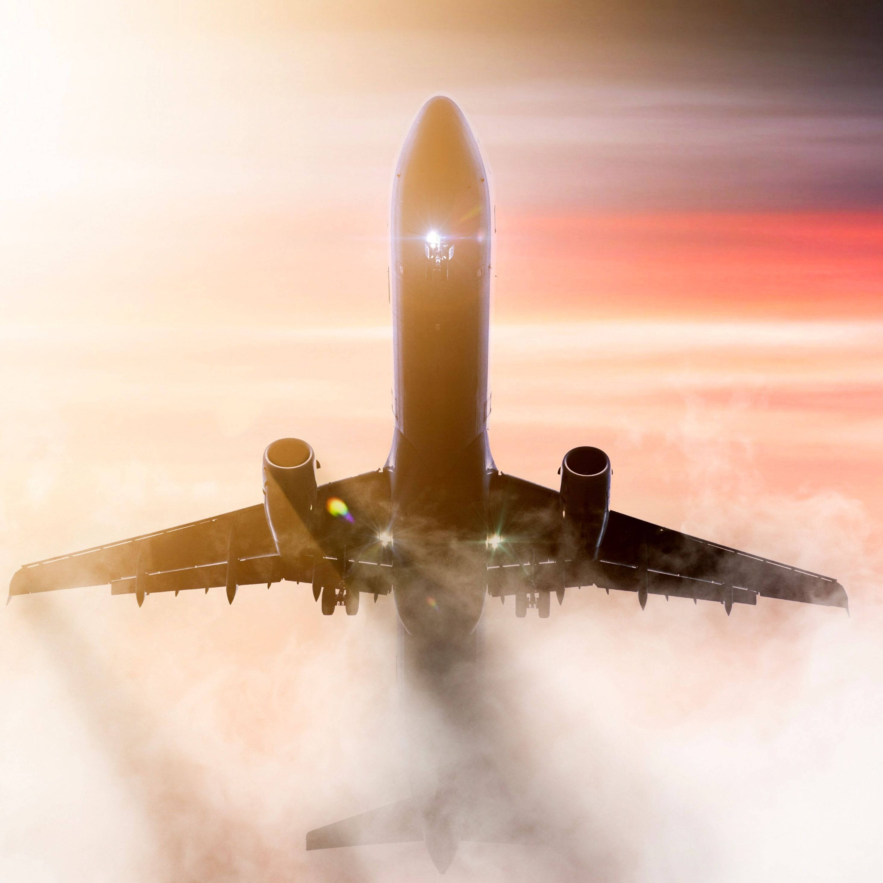 飛機明亮雲朵 壁紙 — 一架商用飛機在日出時翱翔於雲層之上，引擎發光，天空呈現火熱的橙色。