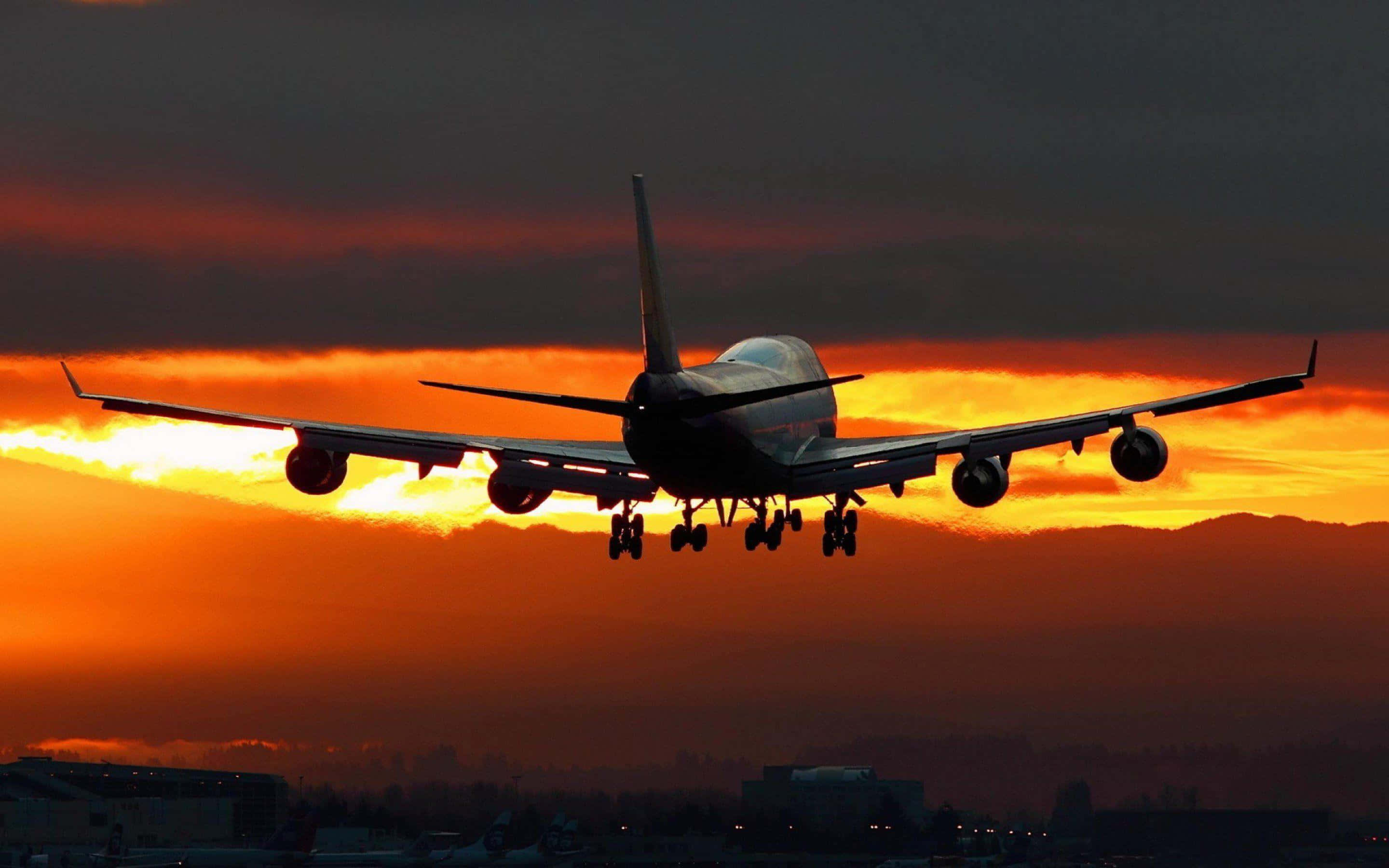 飛機在夕陽下著陸，天空呈橙色，遠處有建築物。