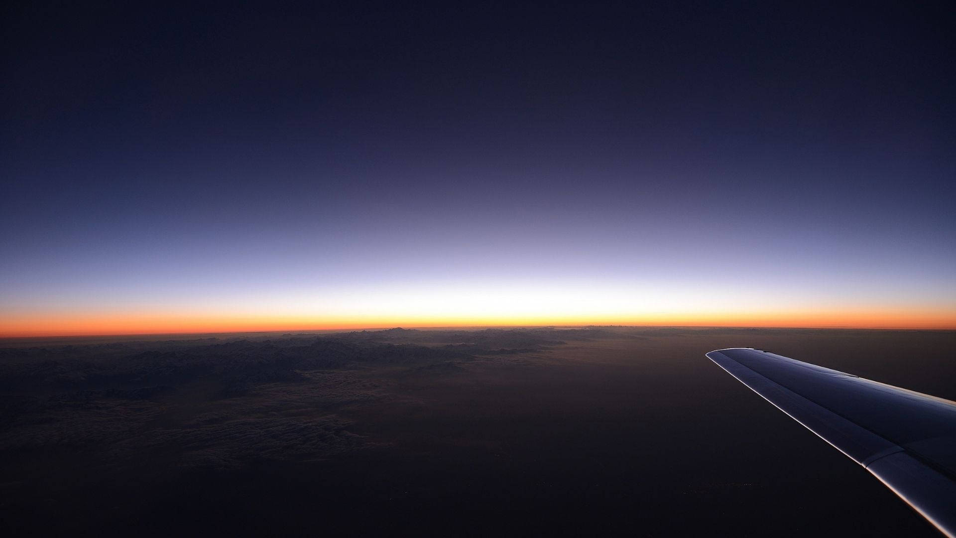 View 桌布 壁紙 — 飛機機翼在暮色天空下呈現剪影，天空在雲層上方帶有橙色和紫色的漸變色調。