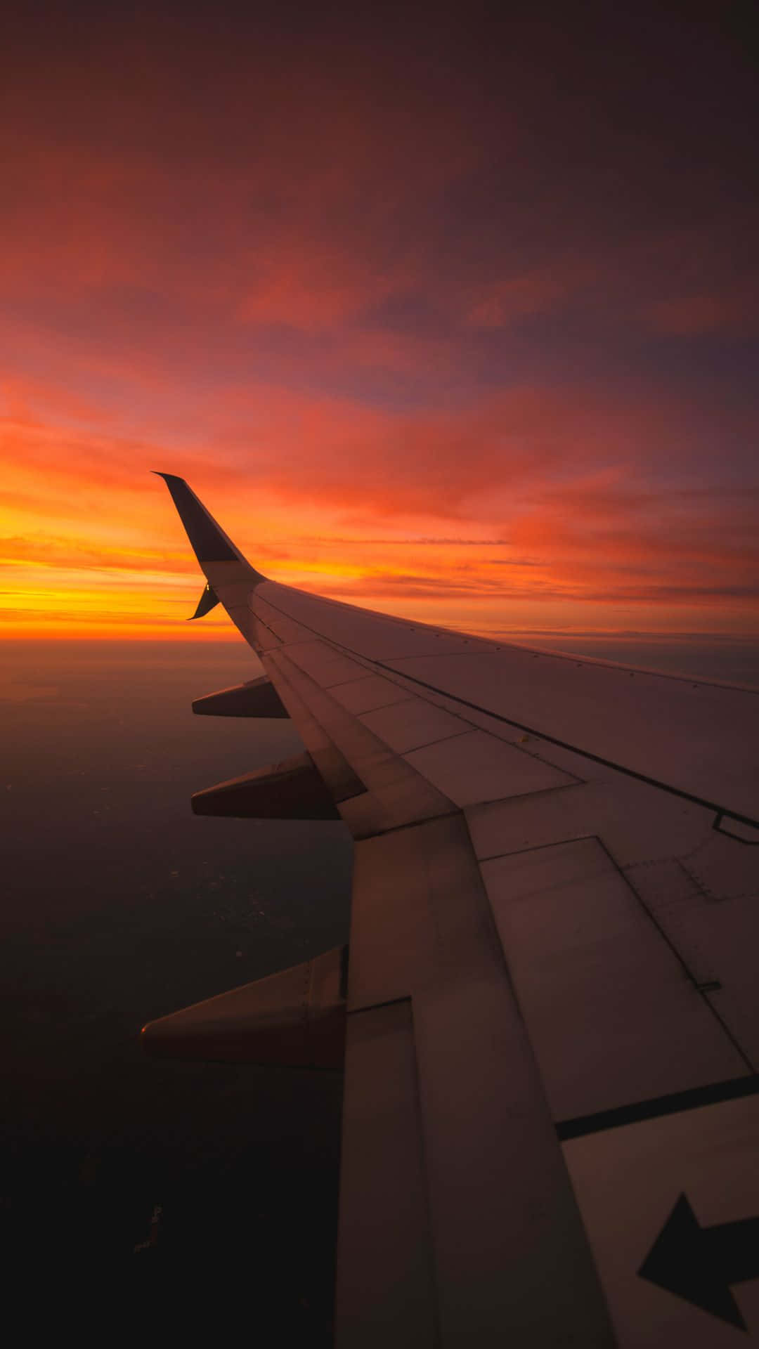 Travel Aesthetic Phone Red Sunset 壁紙 — 飛機機翼在雲層上方火熱的橙色和紫色日落天空襯托下形成剪影。