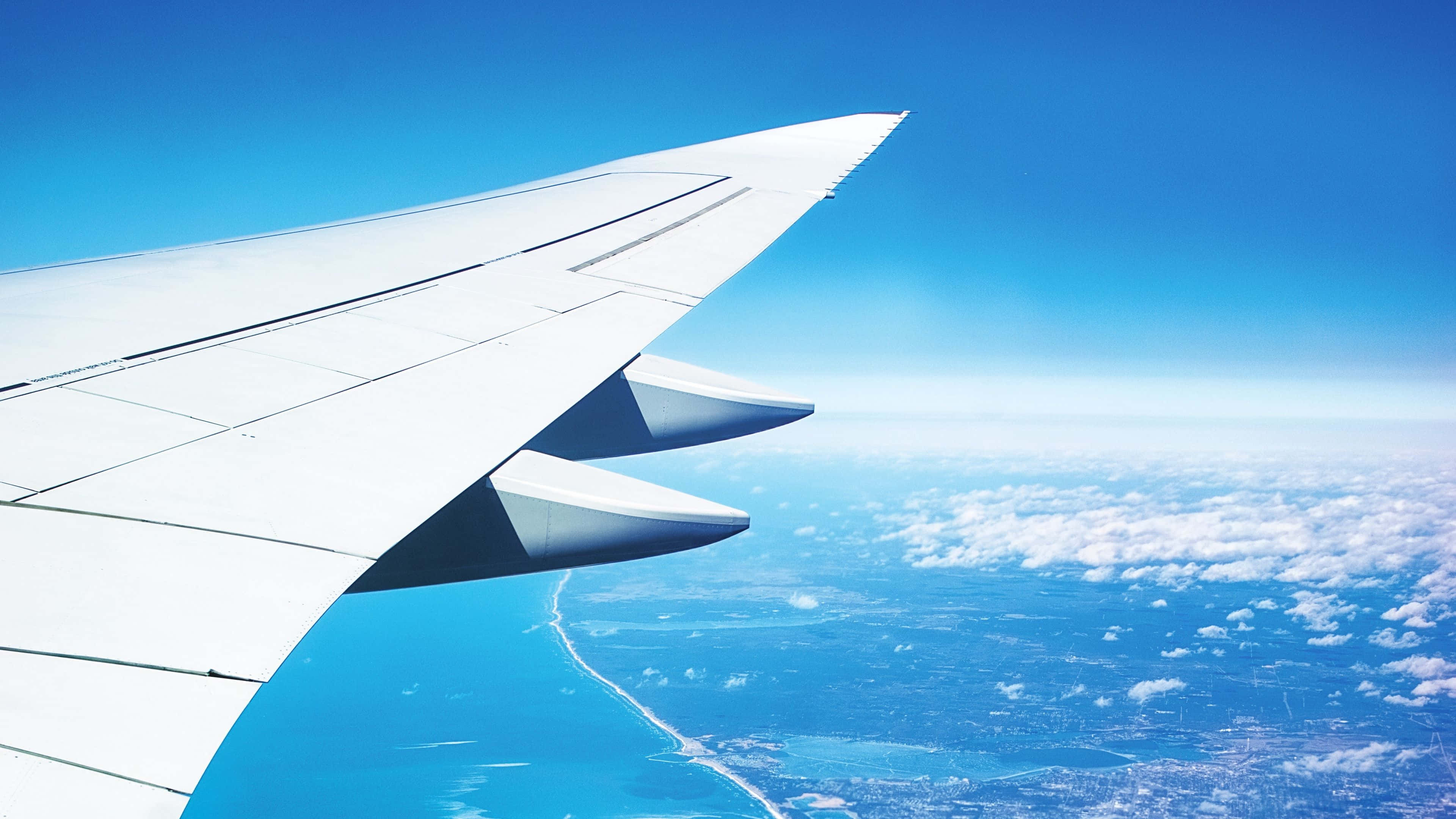 4K 飛機壁紙 桌布 壁紙 — 飛機機翼延伸在碧綠海洋和雲層之上，在清澈藍天下。