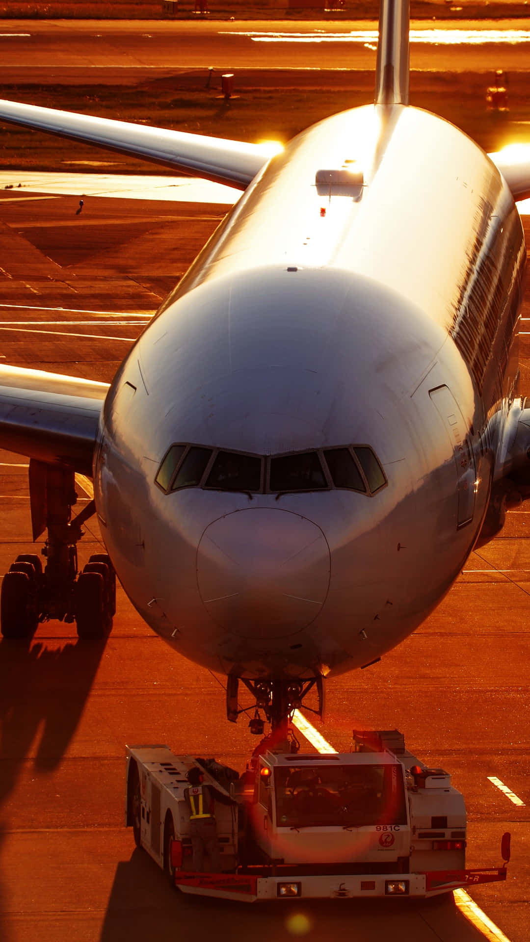 飛機正面視角安卓飛機壁紙 壁紙 — 一架大型飛機正在跑道上被拖行，夕陽溫暖的金色光芒投下長長的影子。