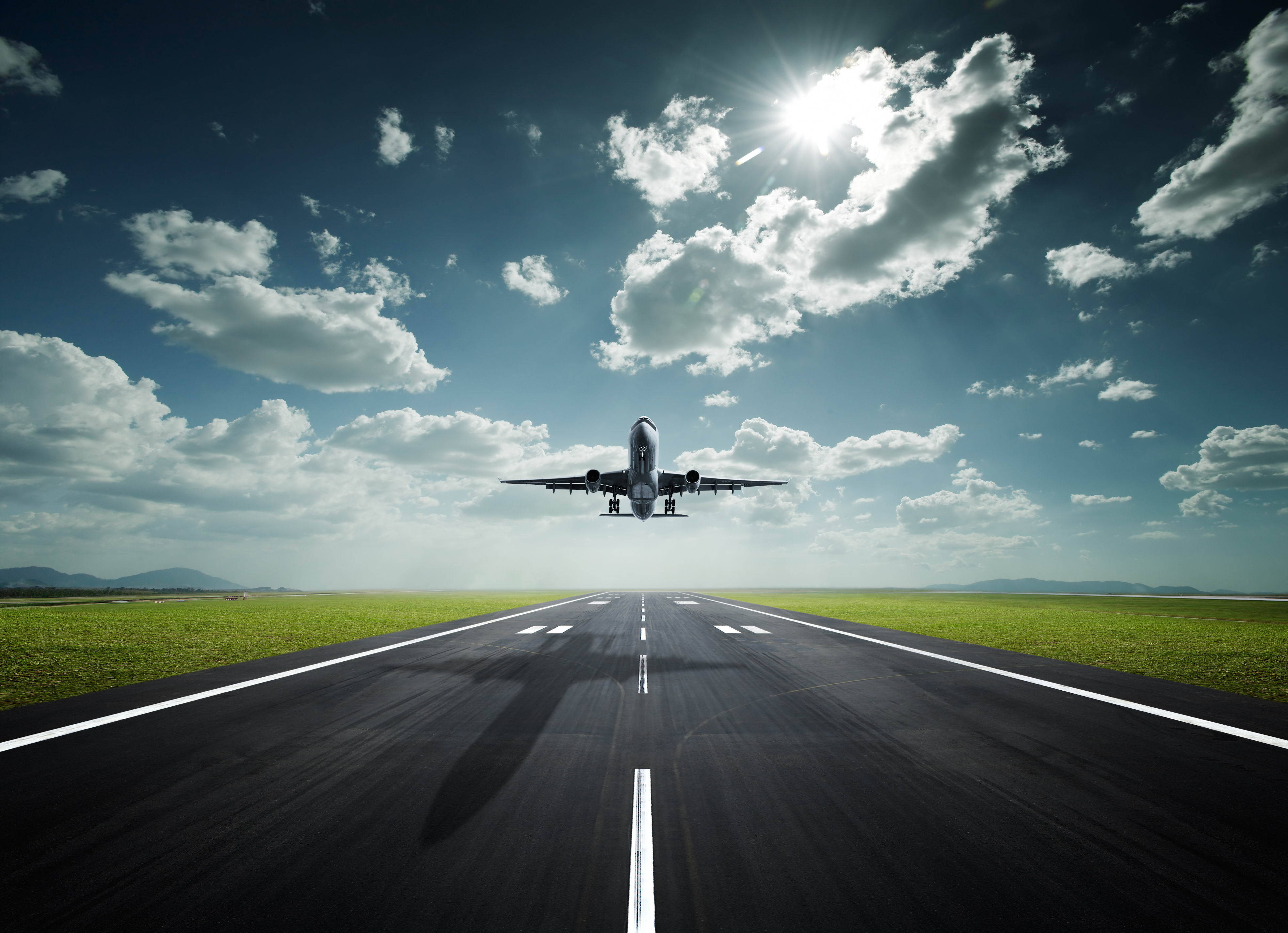 飛機穿越陰雲與陽光 壁紙 — 一架商用飛機在明亮的陽光和散落的雲朵下從跑道起飛。