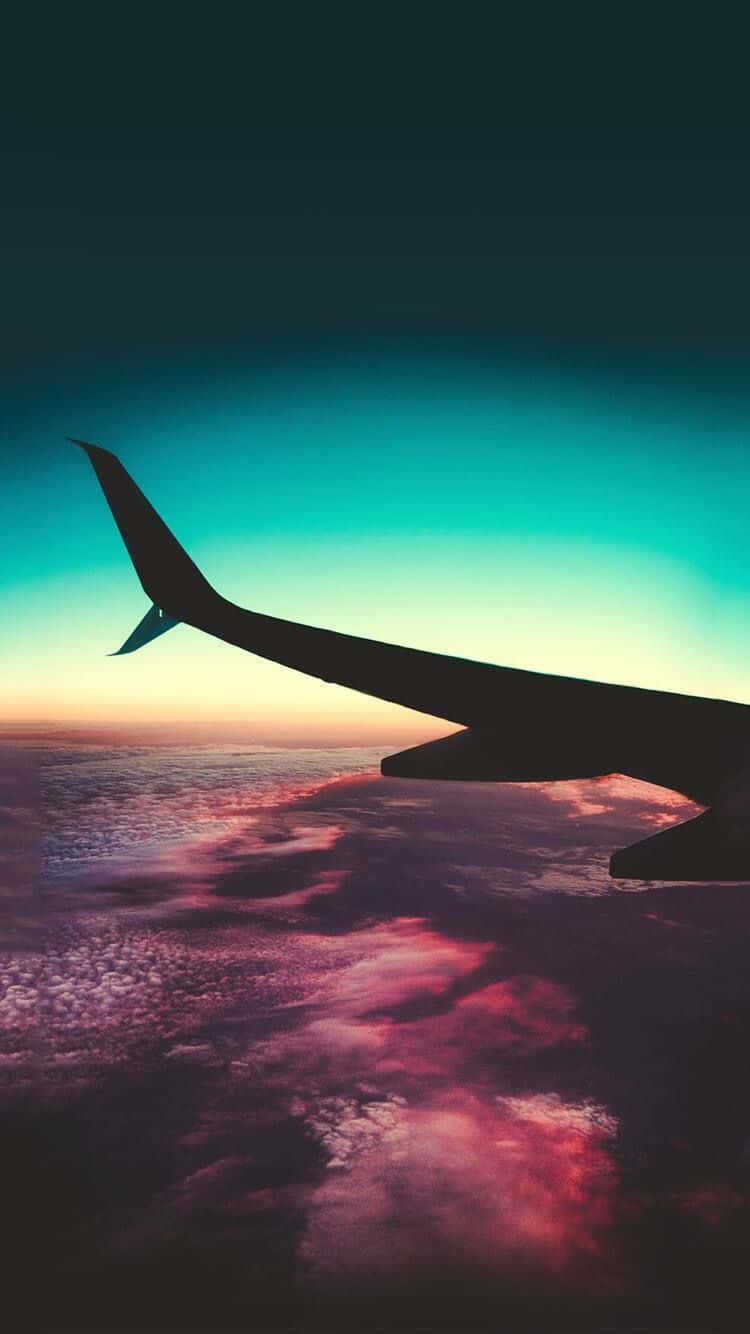 飛機穿過雲層 壁紙 — 飛機翼的剪影，背景是充滿活力的日落天空，下方有粉紅色、紫色和藍綠色的雲。
