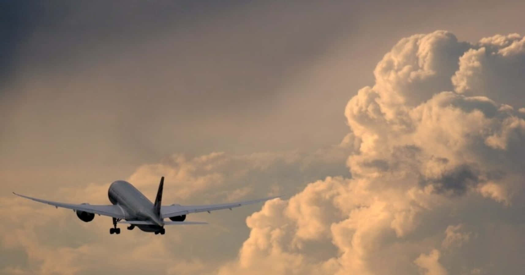 飛機穿雲圖像 壁紙 — 一架商用飛機在日落時分，於充滿金色和灰色雲彩的戲劇性天空下降。