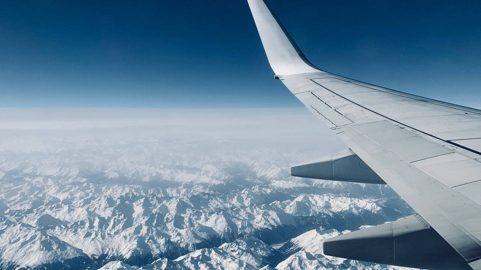 飛機窗外天際 壁紙 — 飛機機翼延伸在廣闊的雪山之上，天空清澈湛藍。