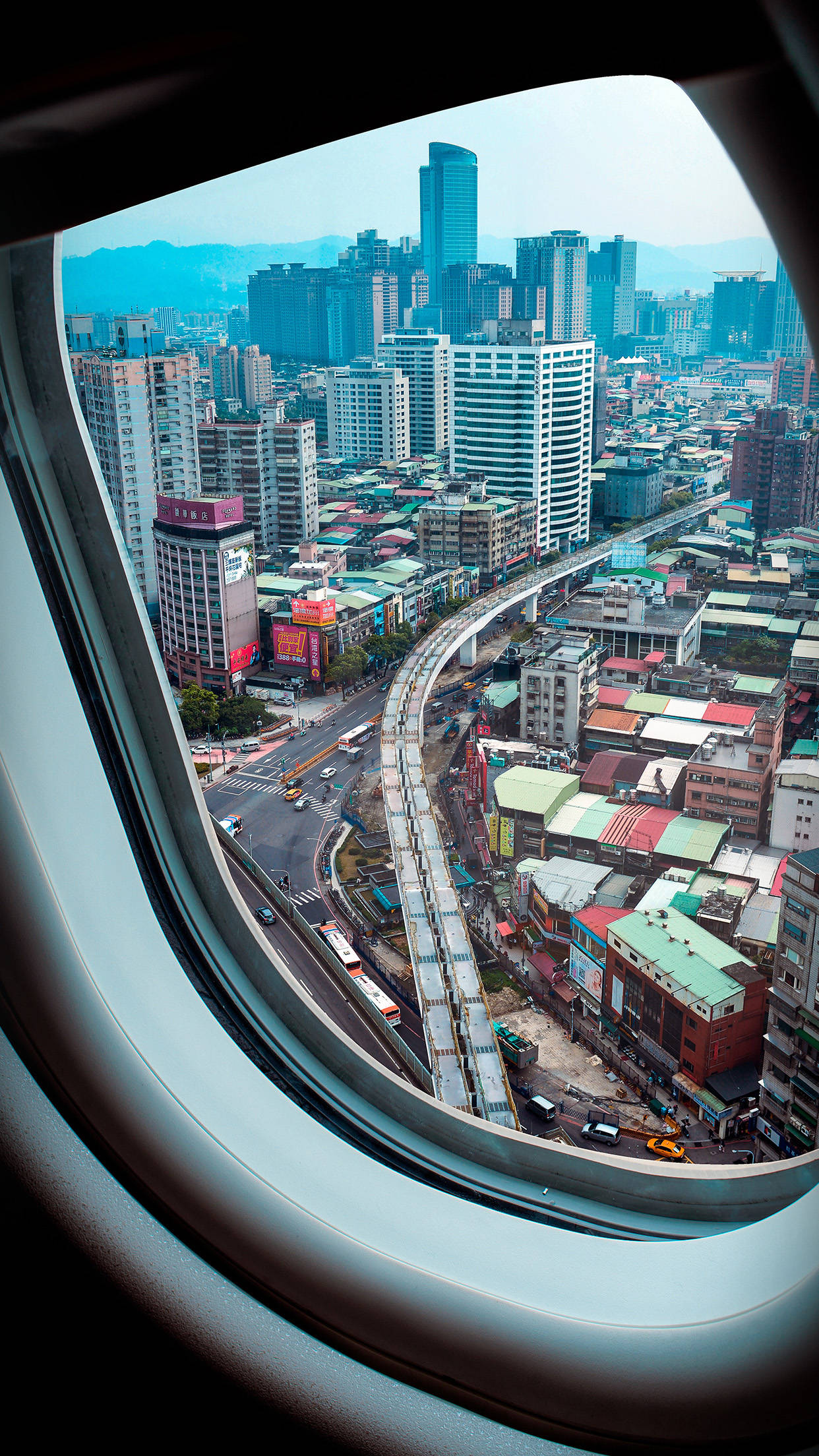 飛機窗戶旅行城市景觀 壁紙 — 從飛機窗戶俯瞰密集的城市景觀，蜿蜒的高架道路和色彩繽紛的屋頂盡收眼底。