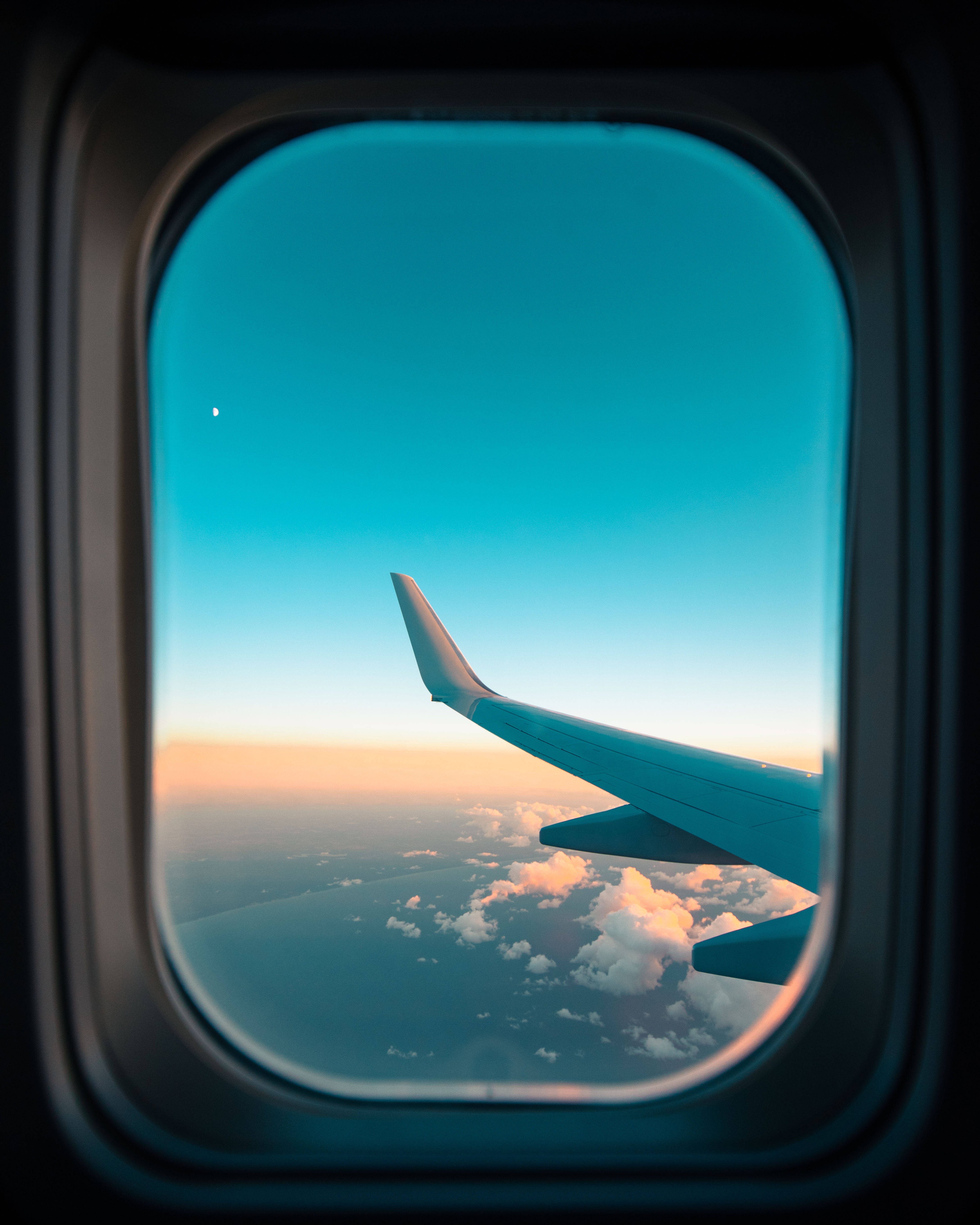 飛機窗戶旅行青綠色系天空 壁紙 — 透過飛機窗戶看到的機翼，伴隨著日落時分發光的雲朵和清澈的藍天。