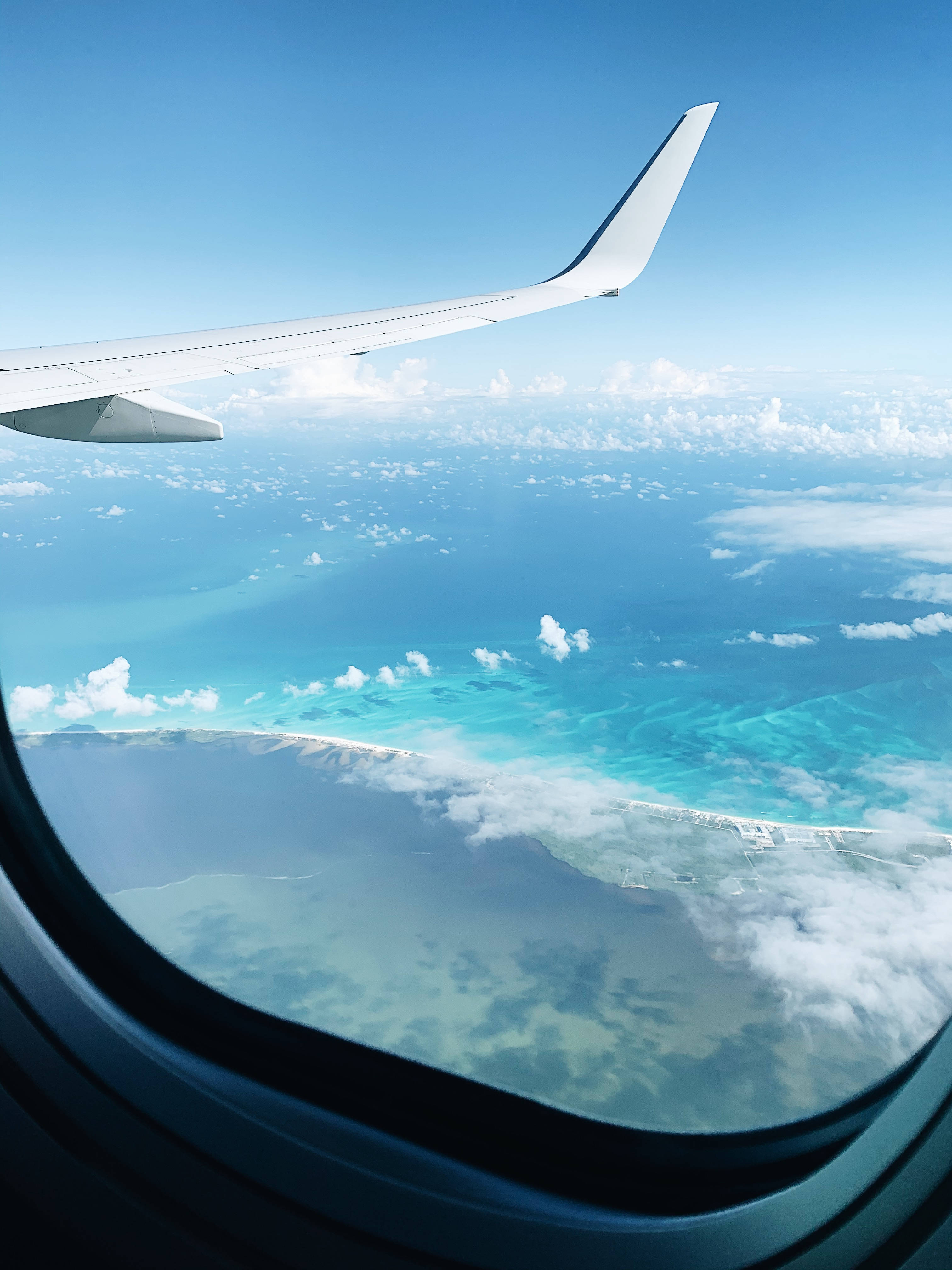 飛機窗戶海天景色 壁紙 — 從飛機窗戶看到的飛機機翼，俯瞰下方的碧綠海洋和白色雲層。