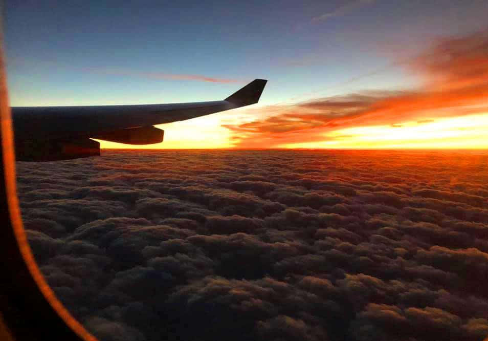 飛機窗戶的天空奇景 壁紙 — 飛機機翼剪影映襯著熾熱的日落，在無盡的棉花雲上將天空染成橙色和藍色。