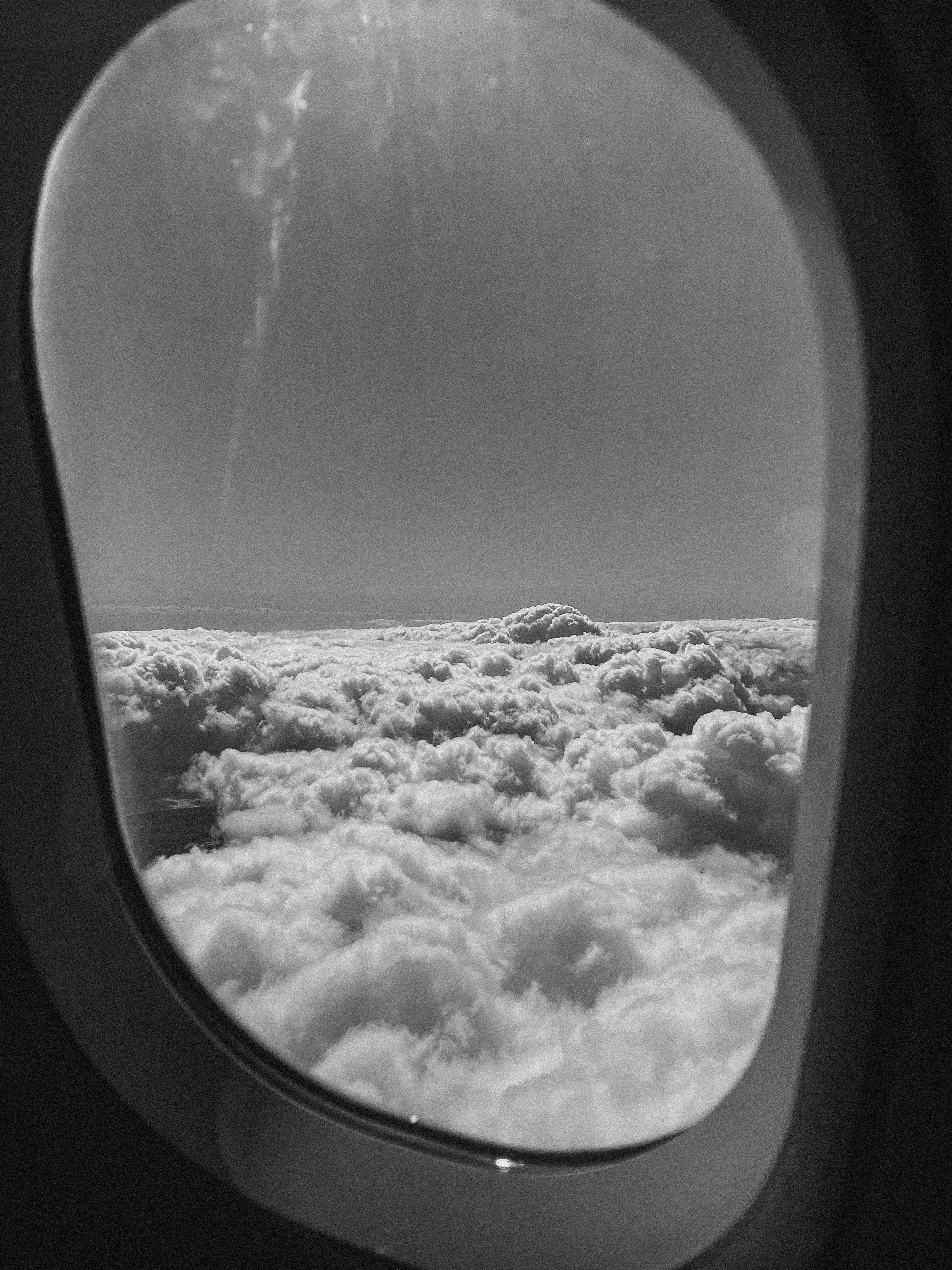 飛機窗戶雲景 iPhone 解鎖畫面 壁紙 — 透過飛機窗戶的黑白景色，展現下方廣闊的 fluffy 雲海，遠方有地平線。