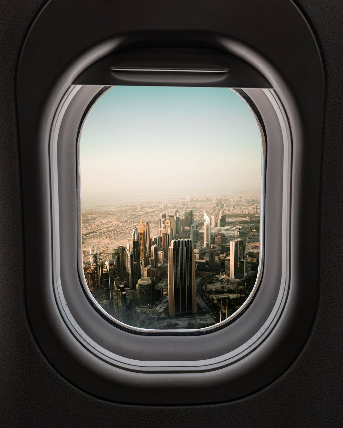 飛機窗邊的城市建築與摩天大樓 壁紙 — 從飛機窗戶看到的密集現代城市景觀的鳥瞰圖，帶有朦朧的金色光線。