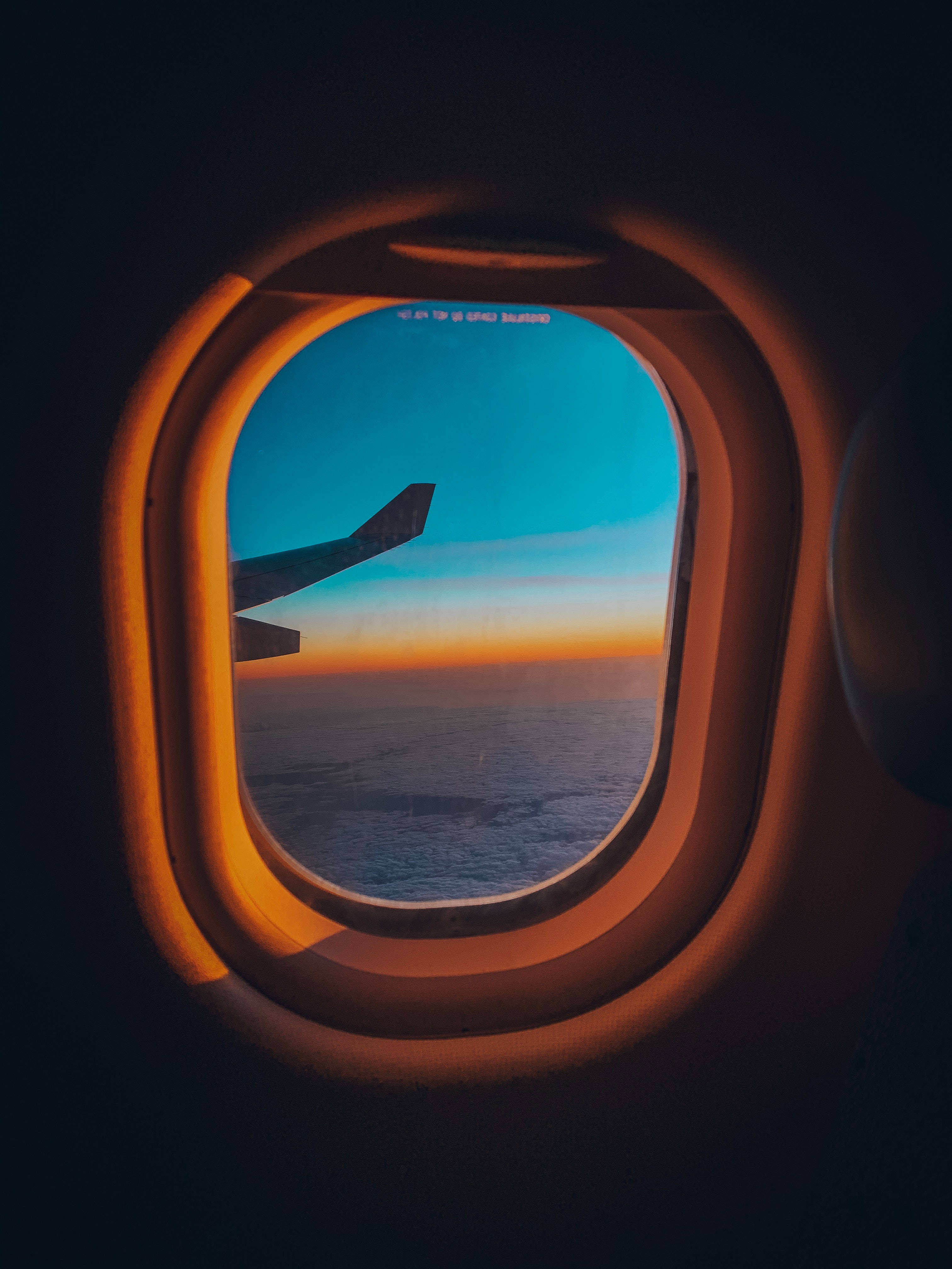 飛機窗邊的夕陽地平線景色 壁紙 — 日落時從飛機窗戶看到的景色，顯示機翼、海洋和漸變天空，由溫暖的機艙燈光框住。