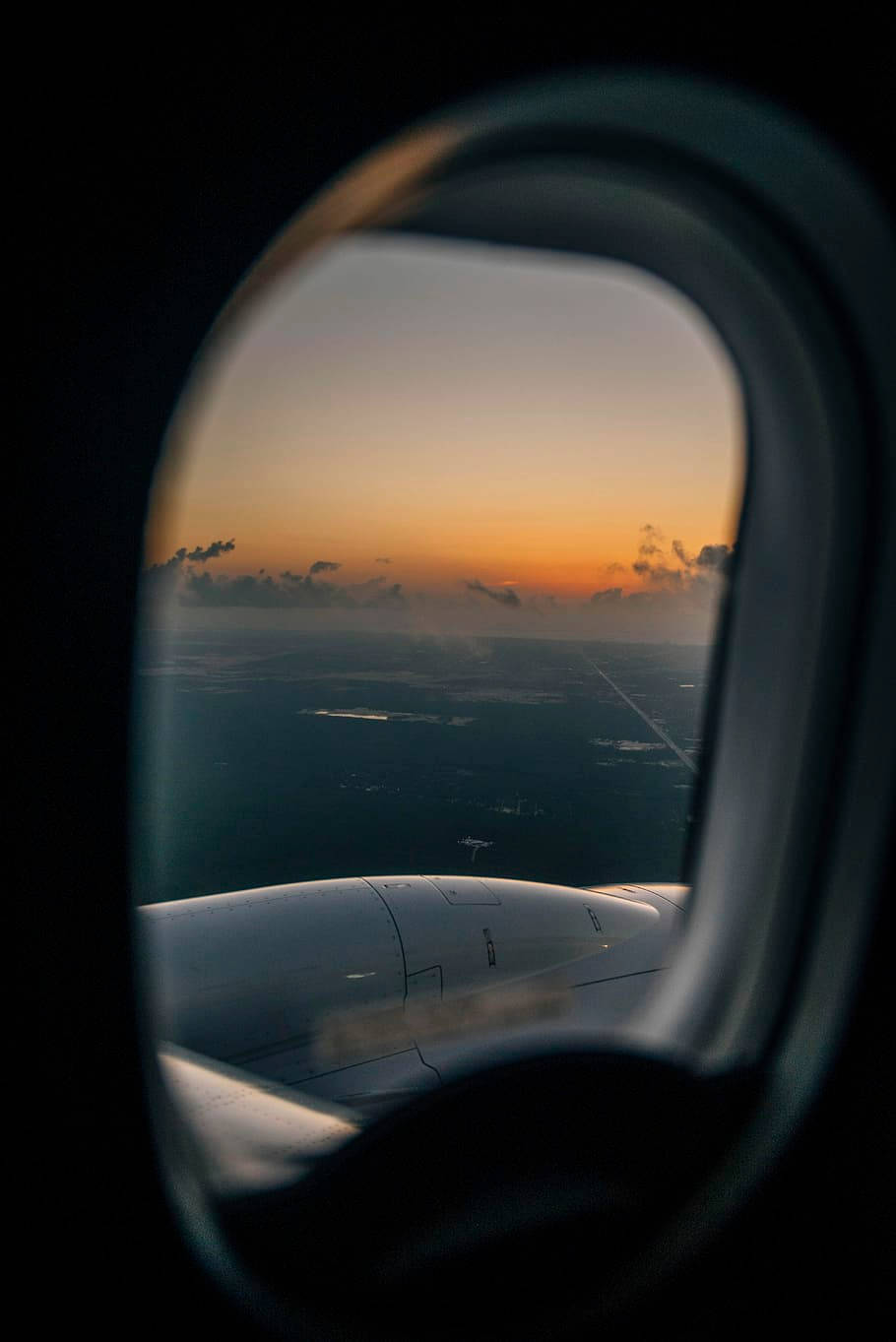 飛機窗邊的夕陽天空景觀 壁紙 — 從飛機窗戶看到的機翼，金色日落映照在雲層和遠處陸地上。