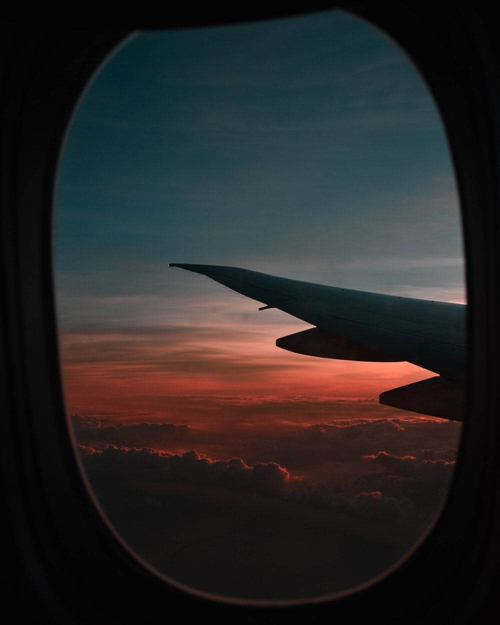 飛機窗邊的復古夕陽旅行風景 壁紙 — 透過飛機窗戶看到的，以熾熱日落天空為背景的飛機機翼剪影。