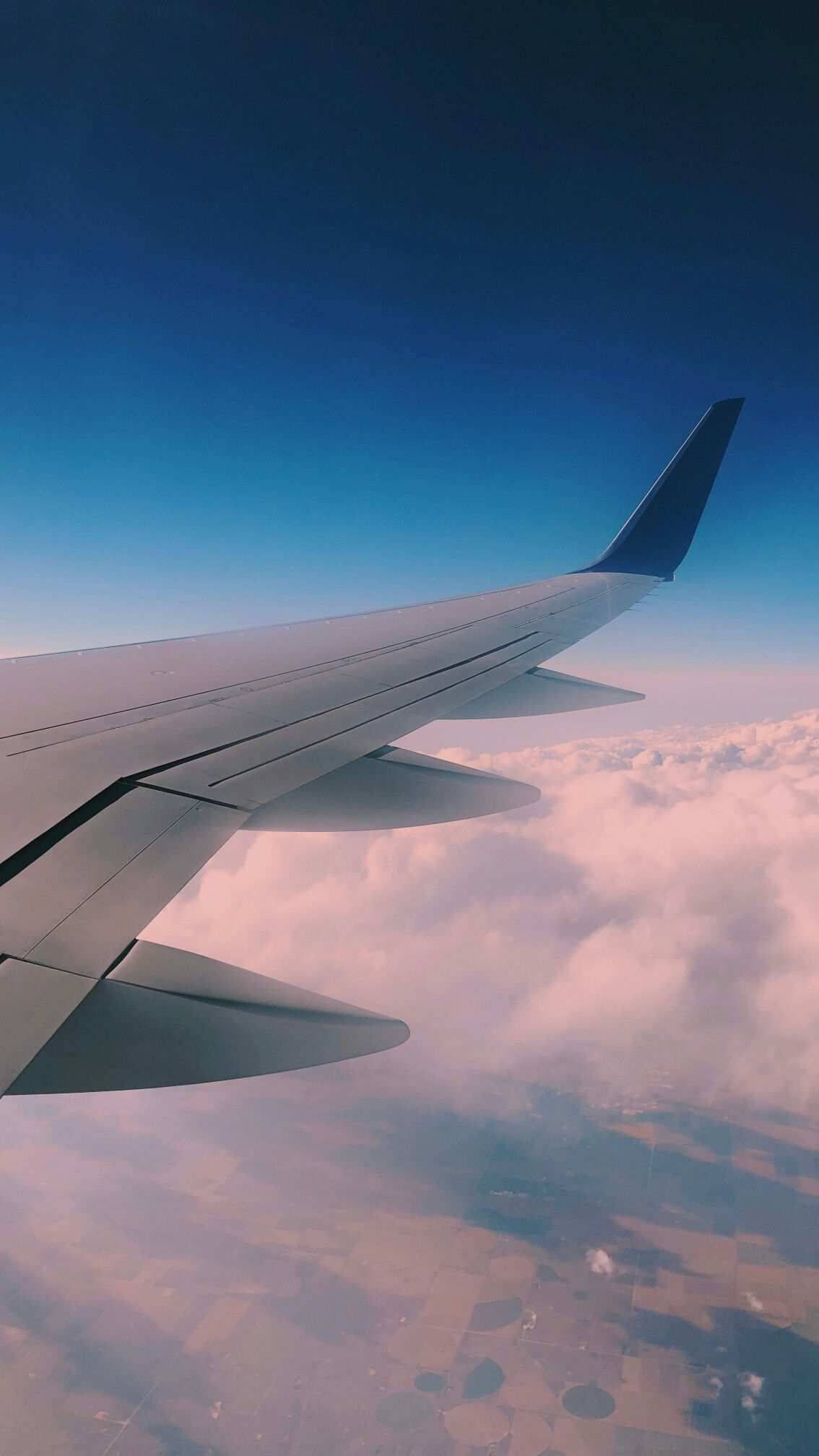 飛機窗邊的旅行雲景 壁紙 — 飛機機翼在漸變藍天下伸展在棉花糖雲層之上，於黃金時段飛行。
