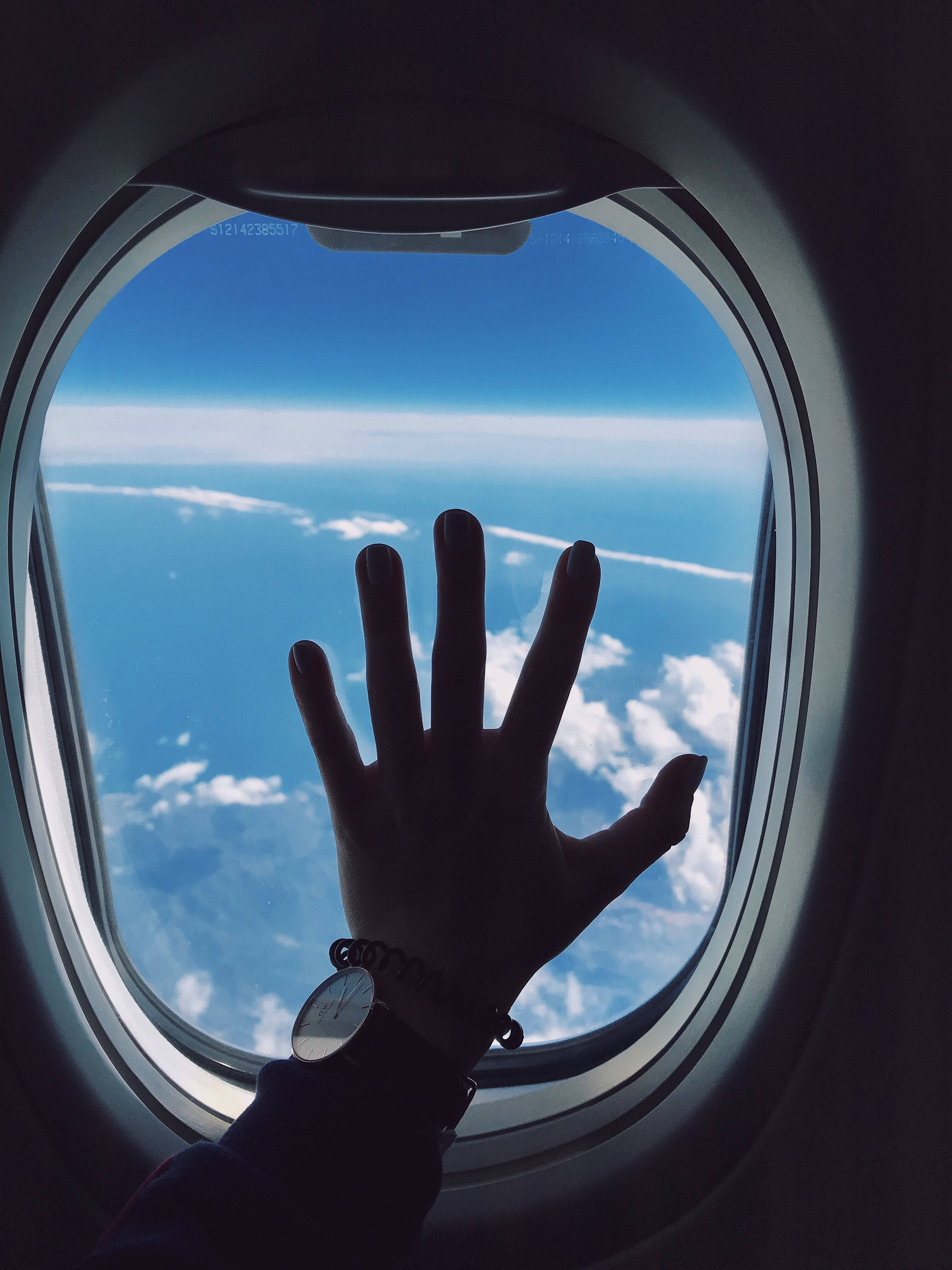 飛機窗邊的流浪手與雲朵風景 壁紙 — 一隻手按在飛機窗上，展現出下方廣闊的藍天和蓬鬆的白雲。