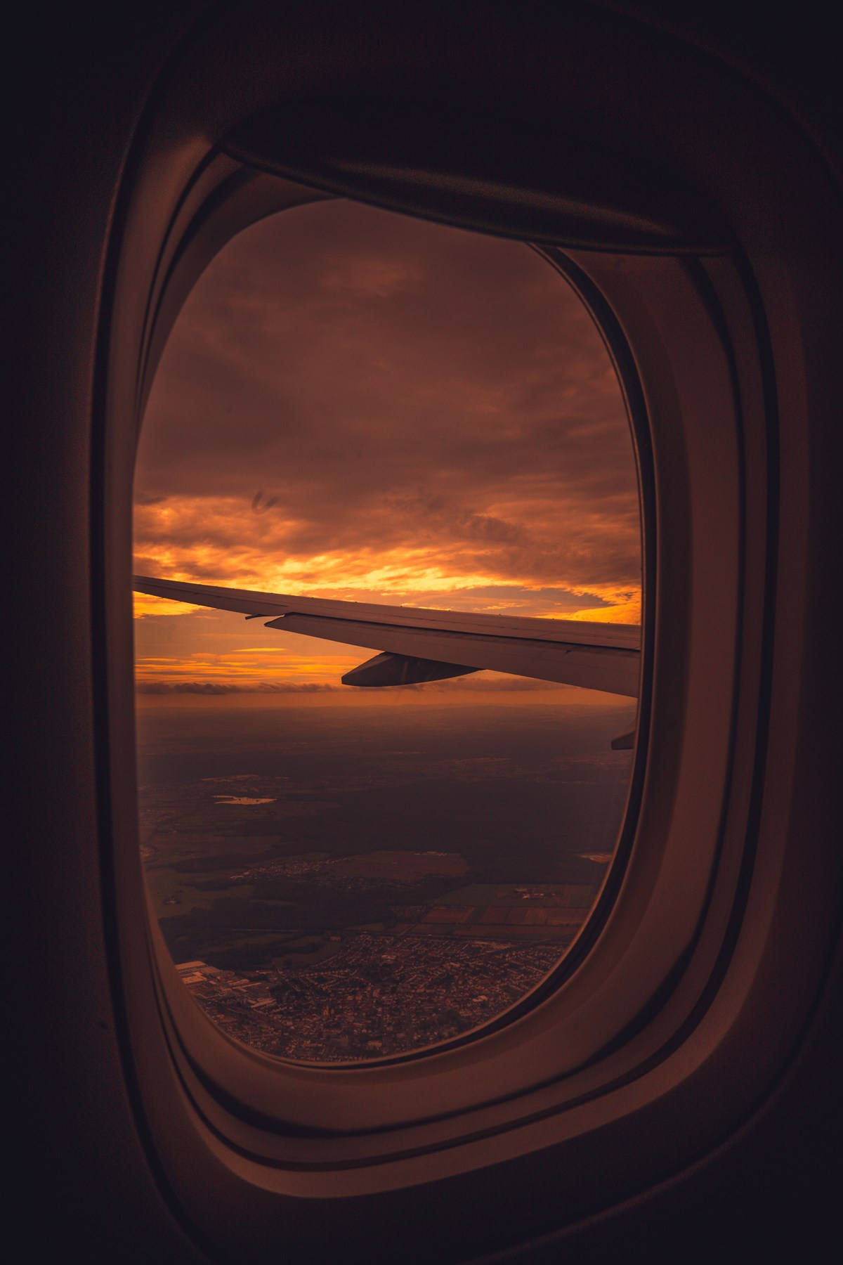 飛機窗邊的紅色夕陽天空 壁紙 — 透過飛機窗戶看到的飛機機翼剪影，背景是火紅的橙色日落。