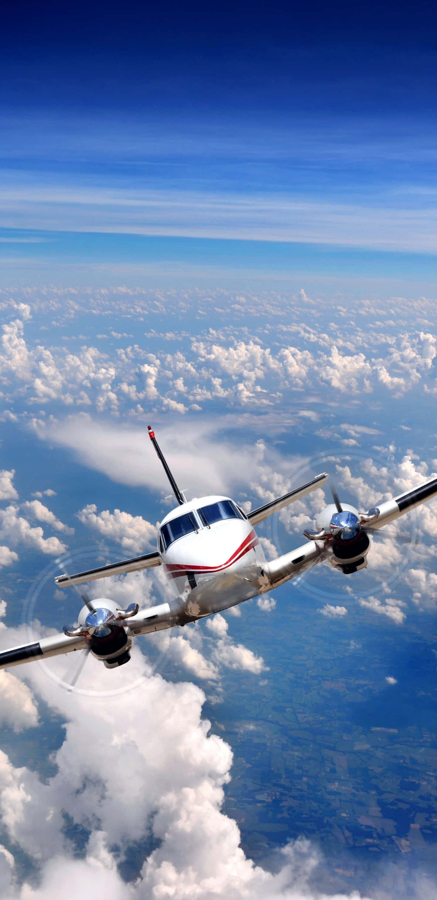 飛機翱翔雲層 Android 背景 壁紙 — 一架白色雙引擎螺旋槳飛機在晴朗的藍天下翱翔於蓬鬆的白雲之上。