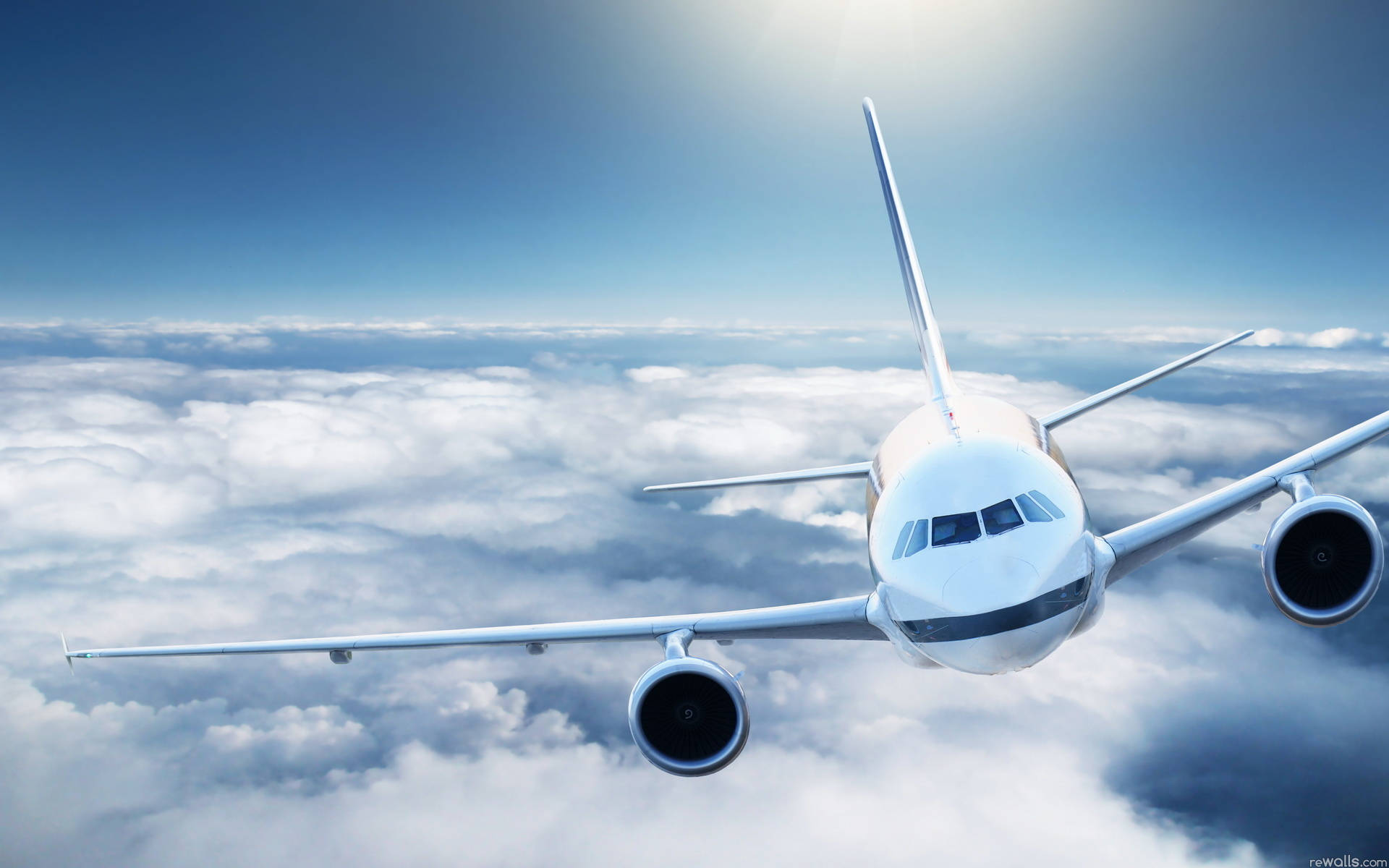 飛機與厚重雲層 壁紙 — 一架白色客機在晴朗藍天和明亮陽光下，翱翔於無盡的蓬鬆雲層之上。