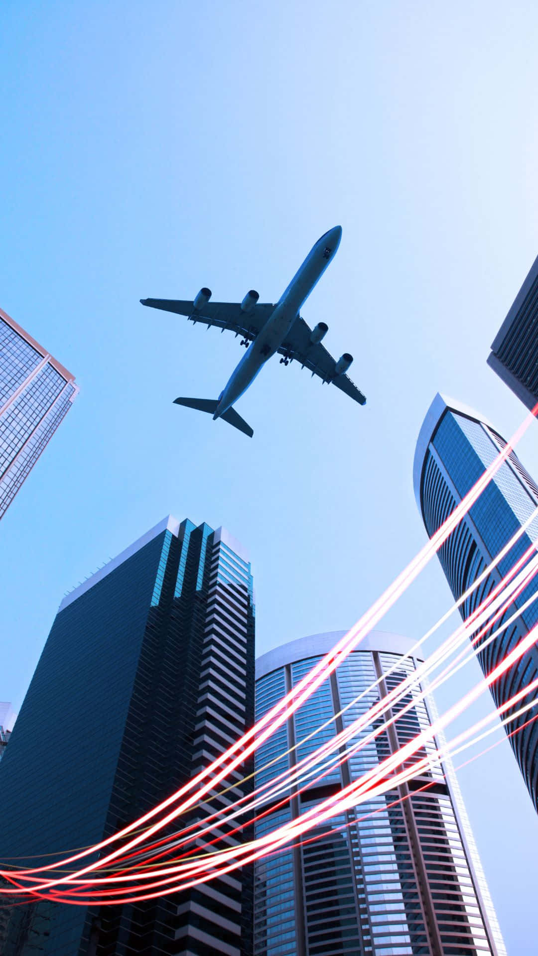 飛機與城市建築背景 壁紙 — 一架商用飛機在晴朗的藍天下翱翔於高聳的摩天大樓之上，下方有紅色光跡。