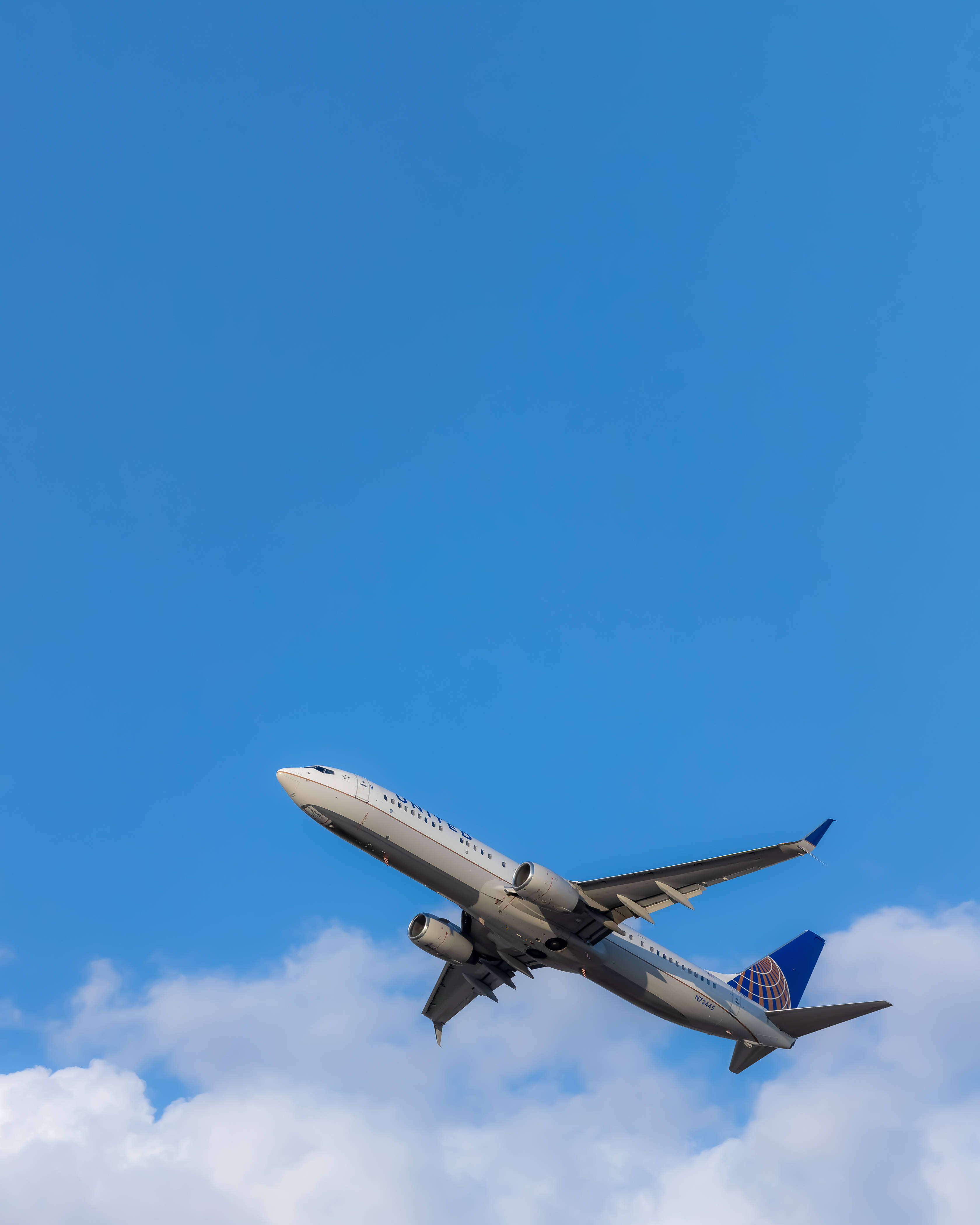 飛機與多雲藍天 壁紙 — 一架聯合航空噴射機在廣闊清澈的藍天和下方蓬鬆的白雲中強力攀升。