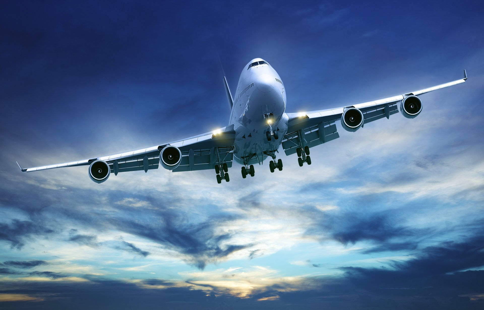 飛機與深藍多雲天空 壁紙 — 一架巨大的白色珍寶客機放下起落架，在佈滿藍色和金色雲彩的戲劇性暮色天空中下降。