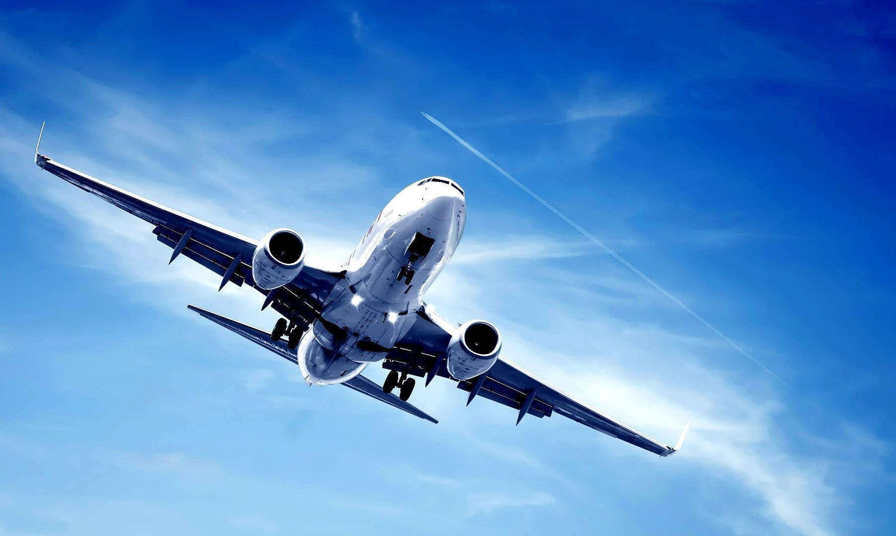 飛機與清澈藍天雲線 壁紙 — 一架白色客機在蔚藍天空中向上翱翔，天空點綴著縷縷薄雲和淡淡的凝結尾跡。