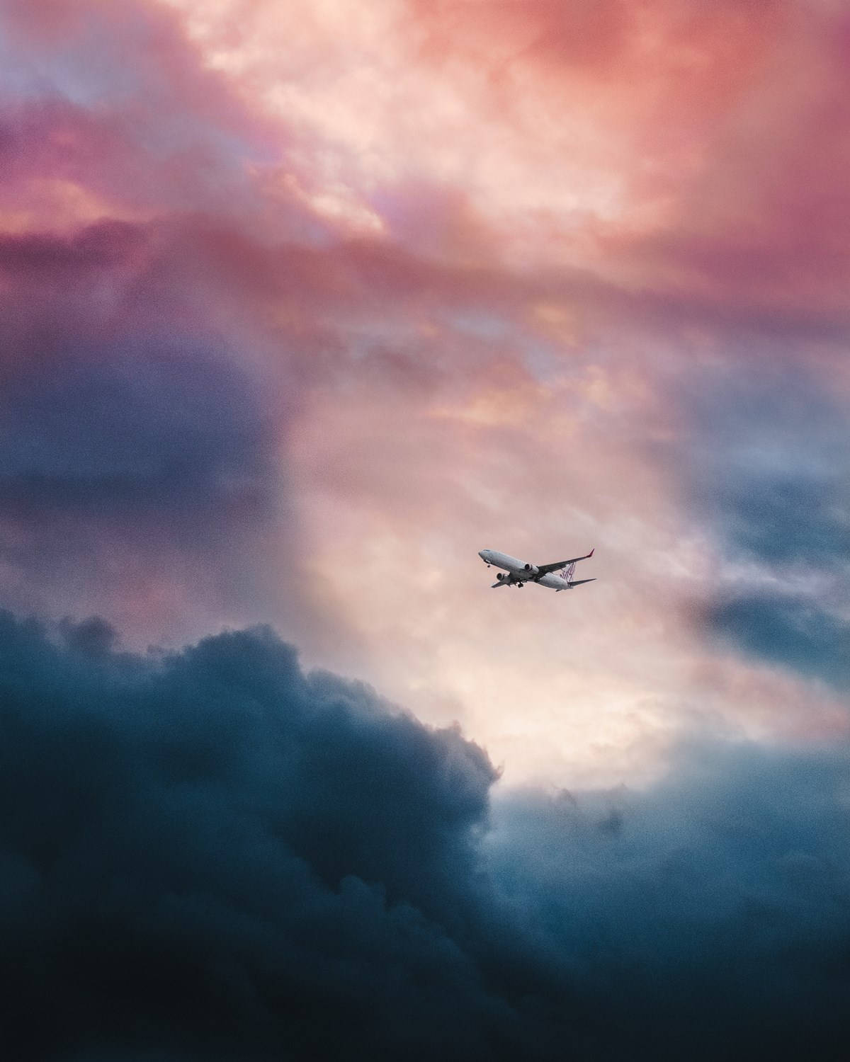 飛機與色彩繽紛的多雲天空 壁紙 — 一架孤獨的飛機在暮色中翱翔，穿越由粉紅、紫色和藍色雲彩繪成的戲劇性天空。