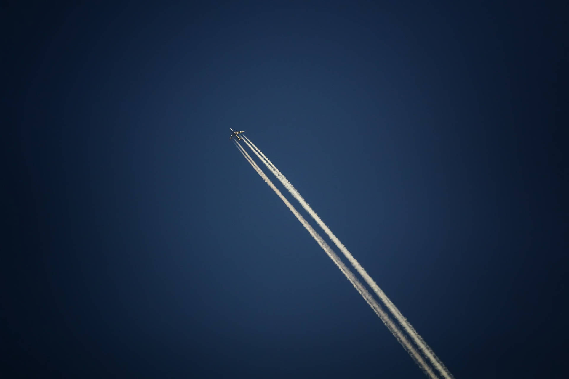 一架飛機在高空飛行，在清澈的藍天上留下兩條白色的凝結尾跡。
