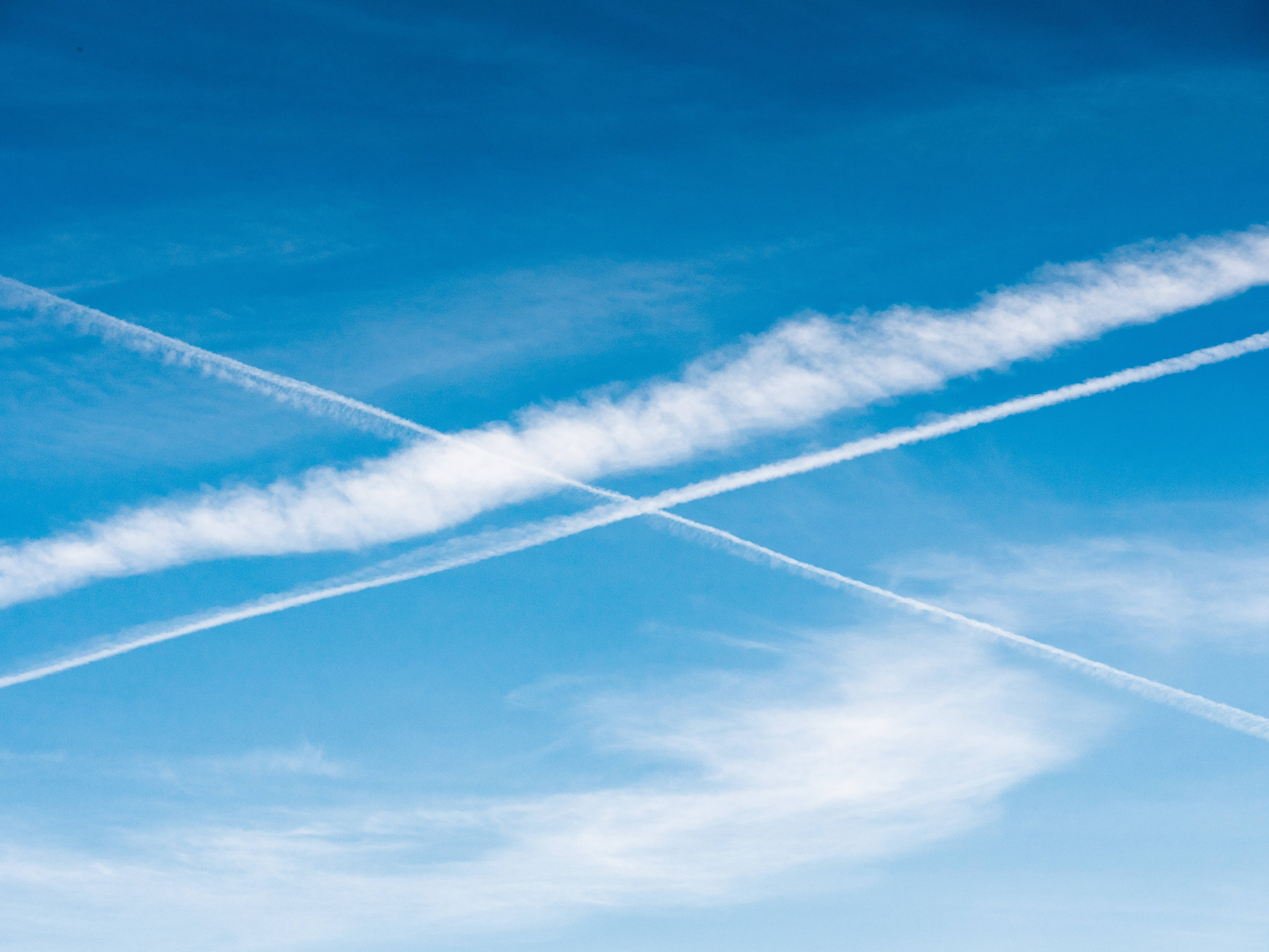 飛機航跡劃過蔚藍天空 壁紙 — 清澈的藍天中，白色的飛機雲交錯形成動態的十字圖案。