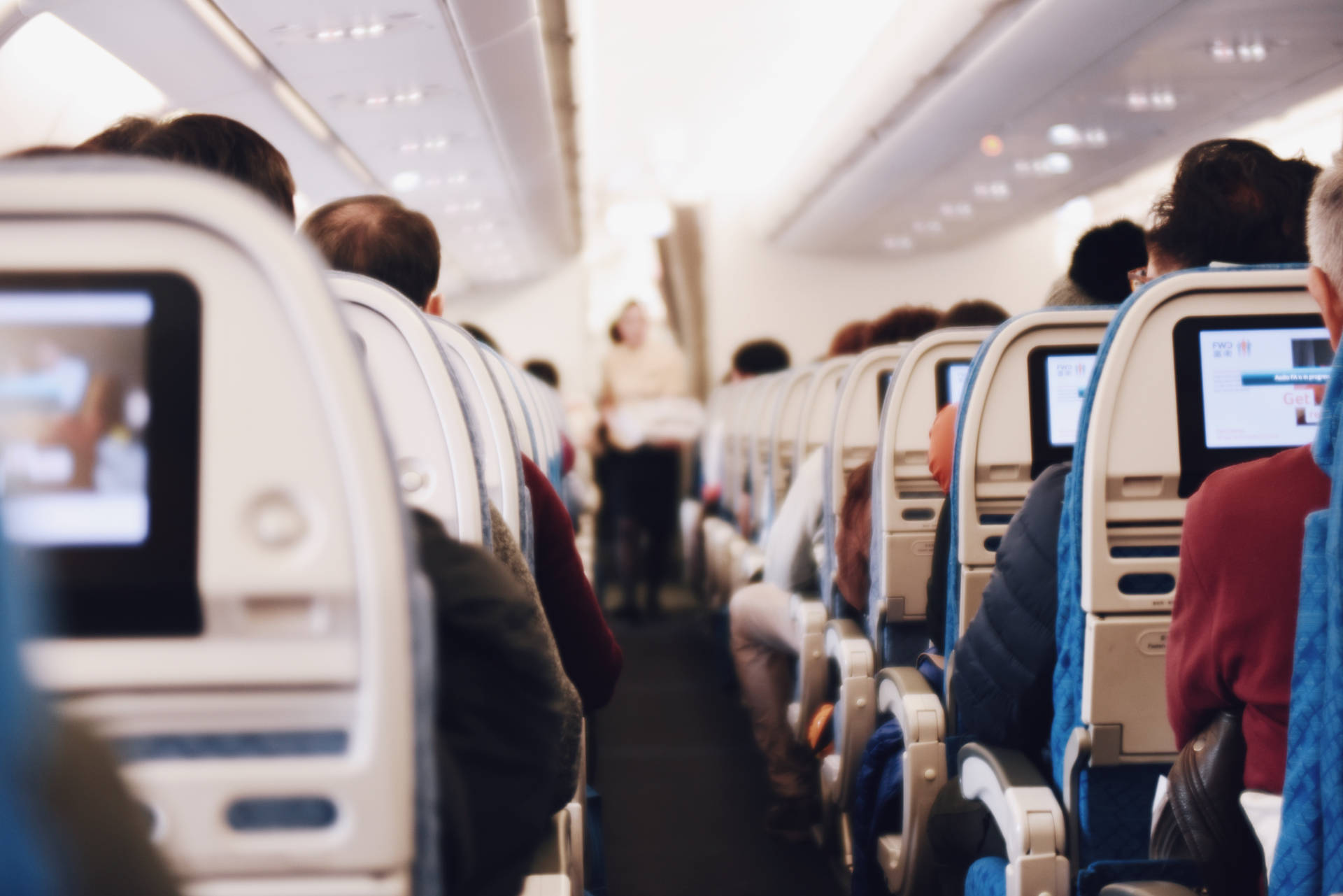 乘客坐在飛機機艙內，個人屏幕亮著，空中服務員正走過通道。