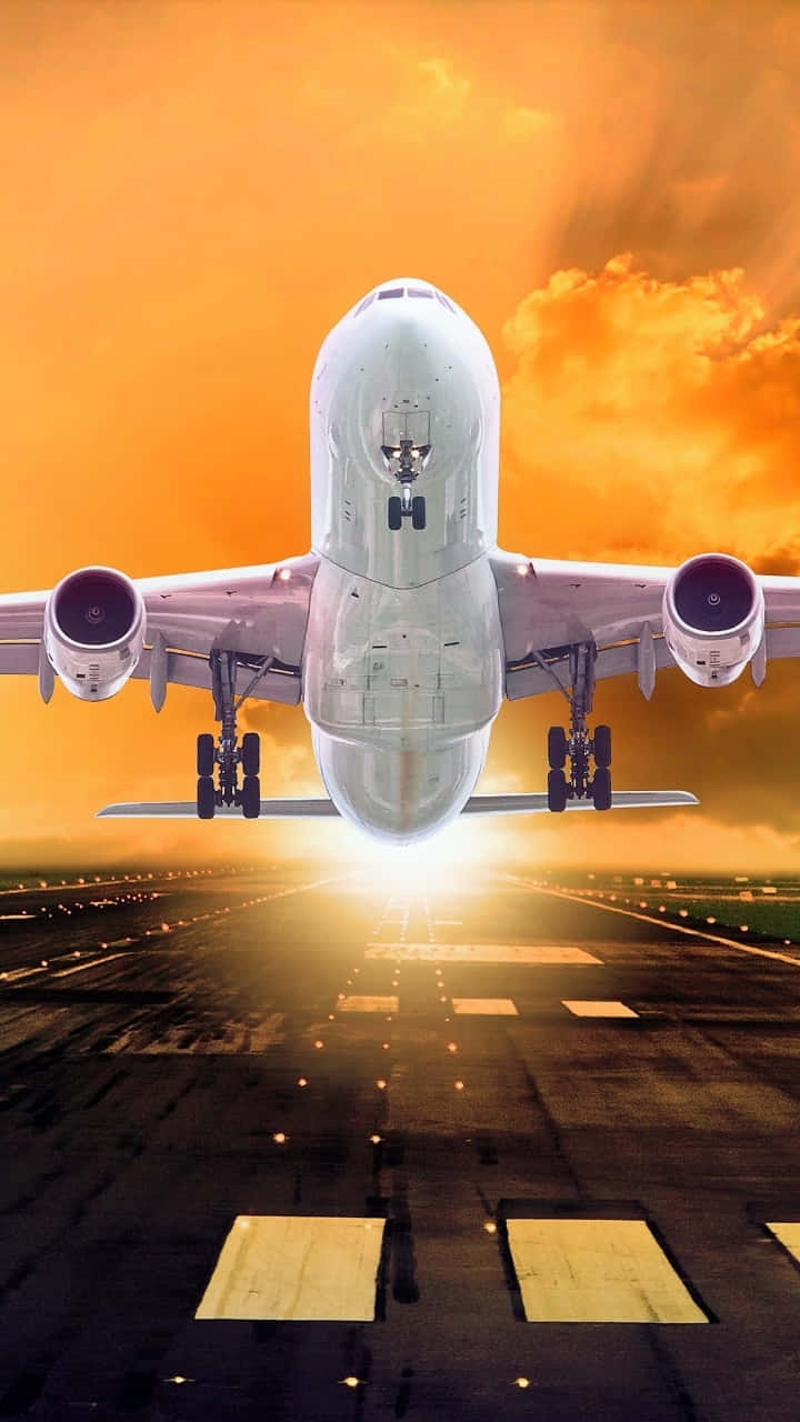 飛機起飛安卓飛機壁紙 壁紙 — 一架大型白色飛機降落到被金色夕陽光芒籠罩的跑道上，上方有戲劇性的橙色雲彩。