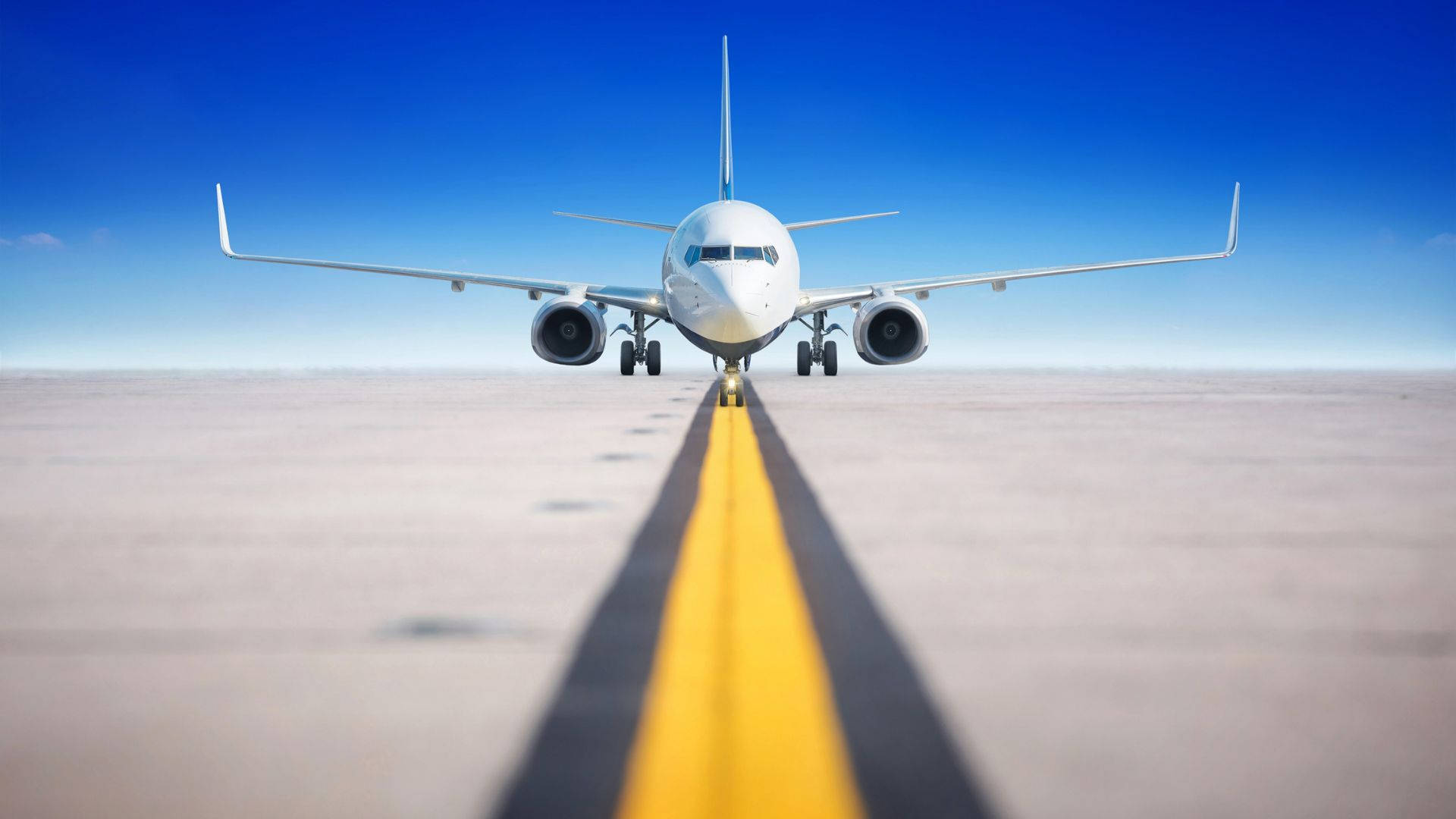 飛機降落於窄跑道 壁紙 — 一架白色客機在跑道上向前，跑道上有醒目的黃色中心線，天空清澈湛藍。
