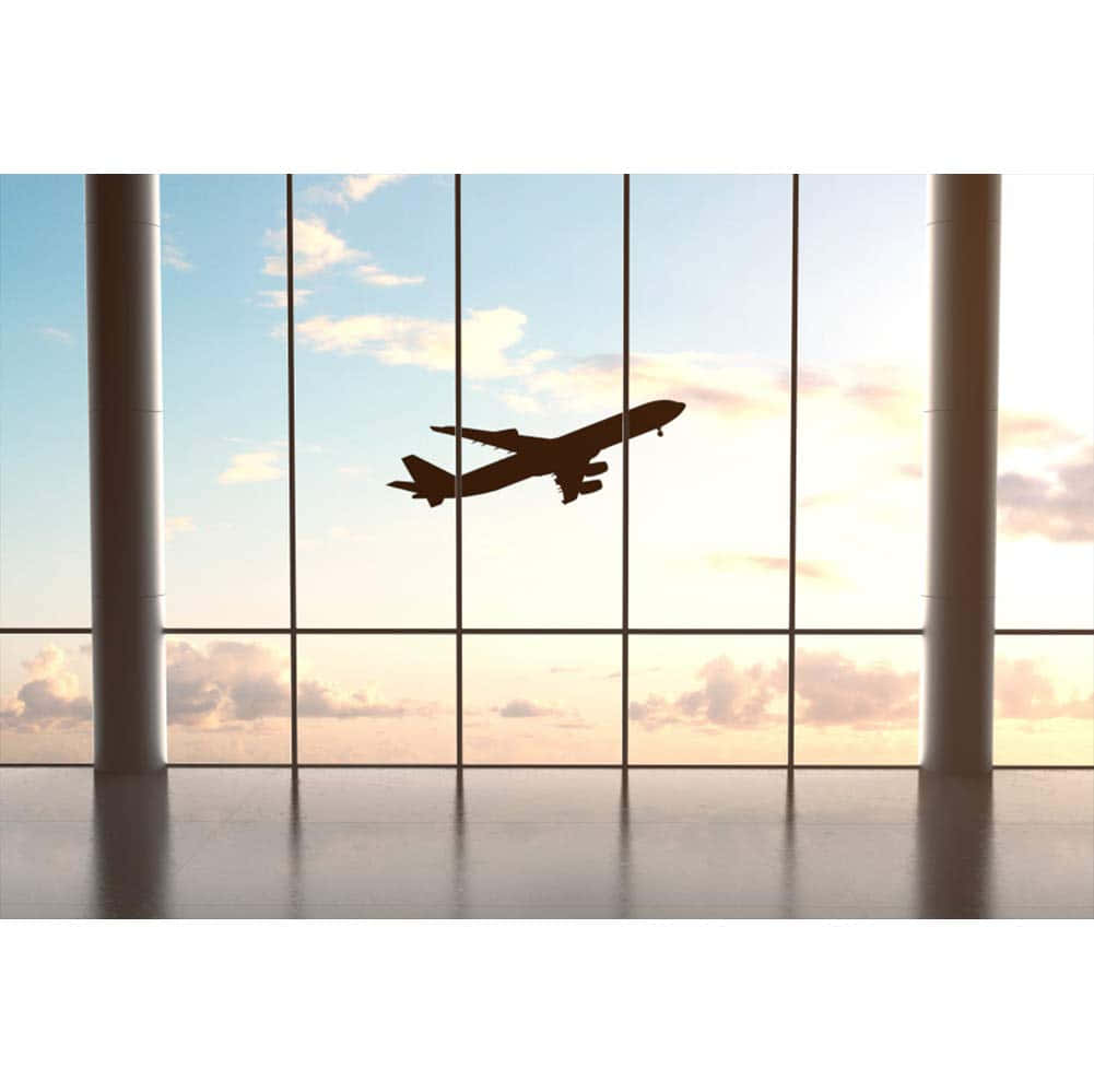 飛機離機後攀升 壁紙 — 透過現代機場客運大樓窗戶看到的客機在日落天空飛行的剪影。
