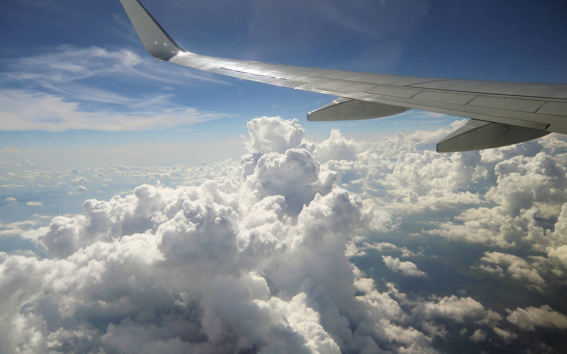 飛機雲景 壁紙 — 飛機機翼在清澈藍天下延伸至蓬鬆白雲之上，從飛機窗戶所見。
