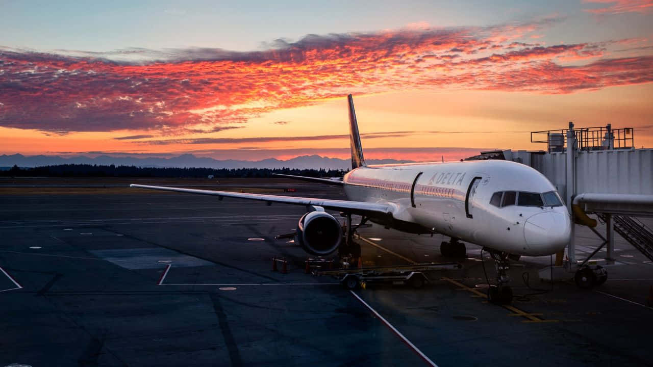 飛機飛行的空中視角 壁紙 — 一架白色阿拉斯加航空噴射機在火熱的橙粉紅色日落天空下，停靠在機場閘口。