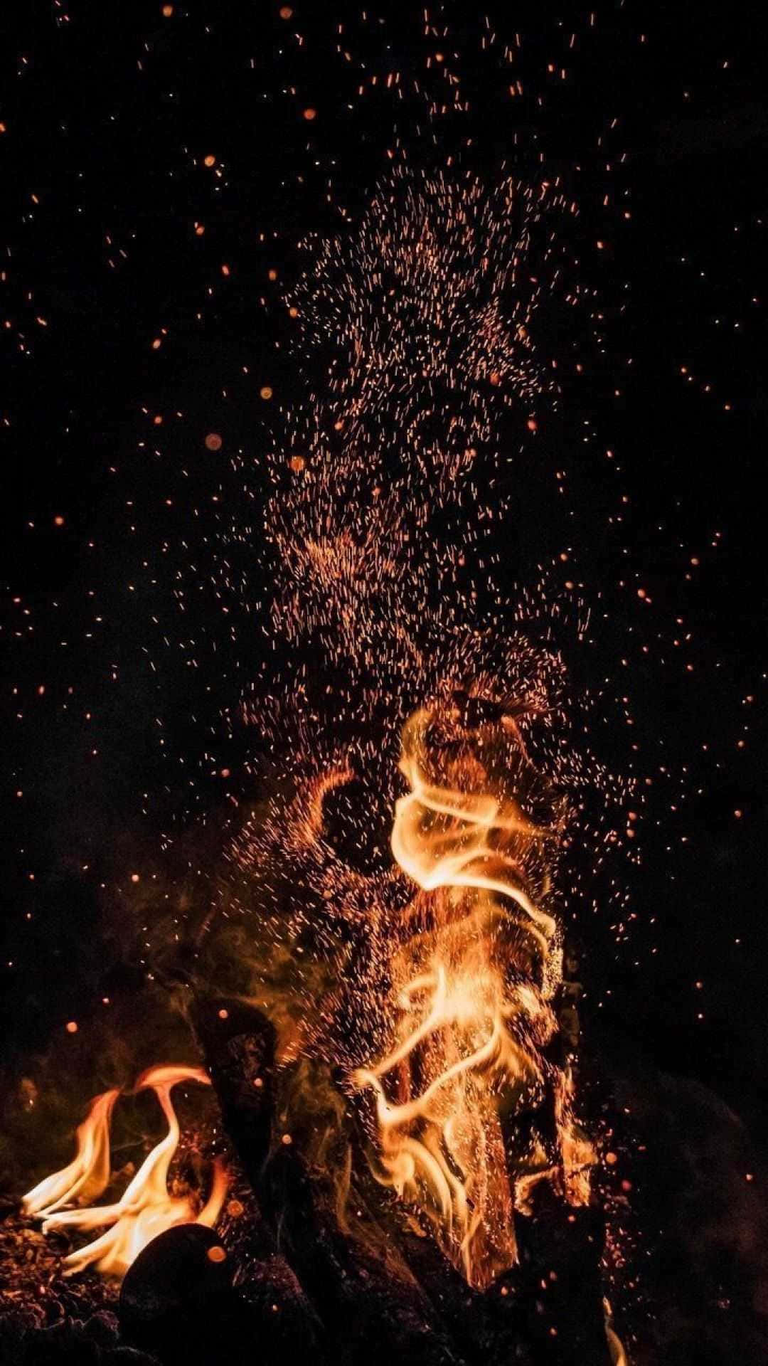 飛舞火星的營火 壁紙 — 鮮豔的橙色火焰和發光的餘燼在漆黑的夜空中向上爆發，形成動態的火焰展示。