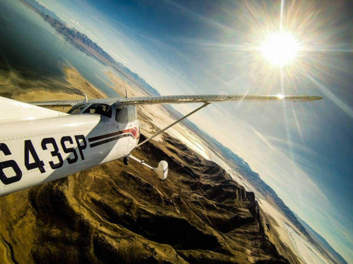 飛行中的飛機尾部 GoPro 壁紙 — 一架小型白色飛機在崎嶇的沙漠地形上空低飛，頭頂太陽猛烈照耀。