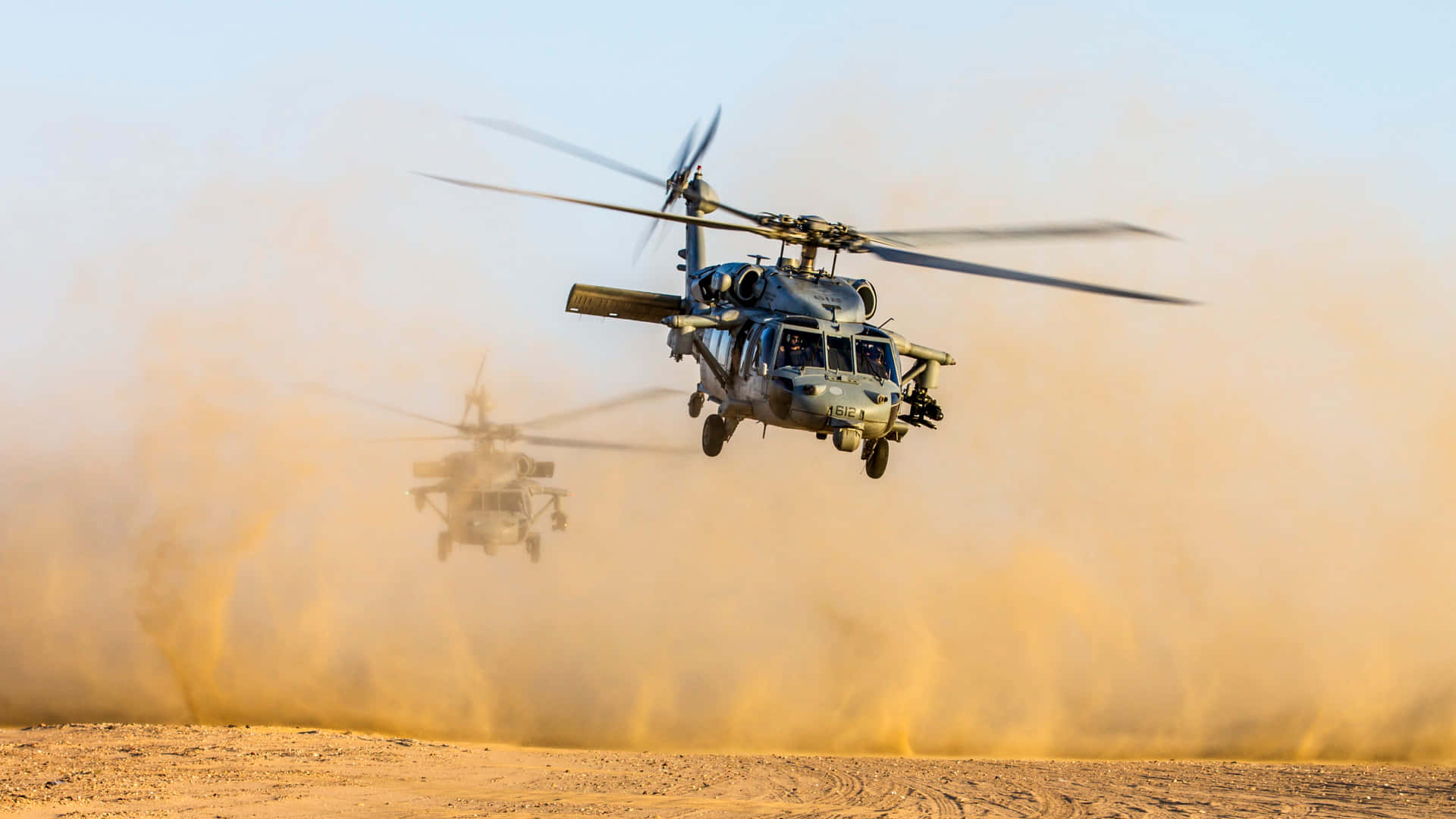 兩架軍用直升機低空飛越塵土飛揚的沙漠景觀。