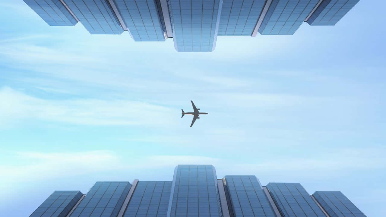 飛行員穿雲飛行，被美景驚嘆 壁紙 — 一架孤獨的飛機在淡藍色天空和薄雲下，飛翔於高聳的玻璃摩天大樓之間。