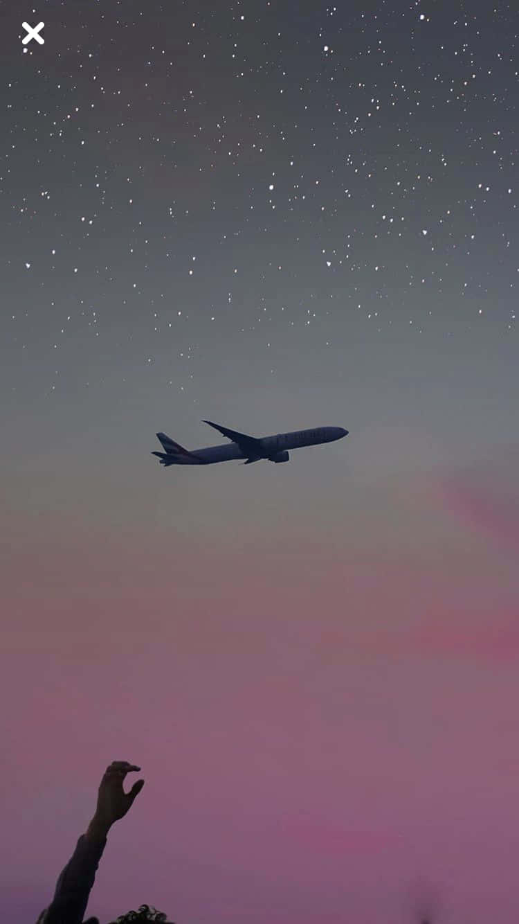一隻手伸向在星夜粉紅和紫色天空下飛行的飛機。
