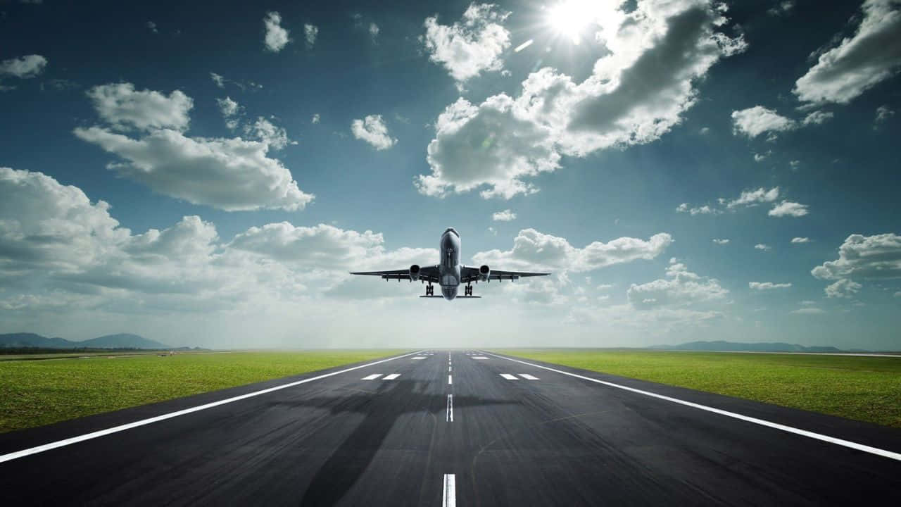 飛越城市上空 壁紙 — 一架商用飛機在明亮的陽光和零星雲朵下從跑道上升。
