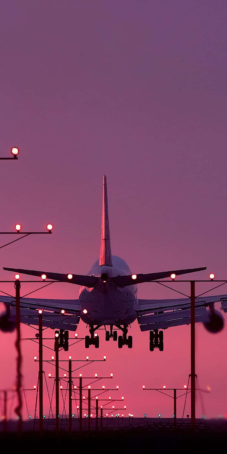 飛機在黃昏時分降落，發光的跑道燈光映襯著粉紫色的天空