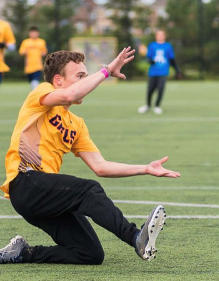 飛躍高處的 Ultimate Frisbee 壁紙 — 一名身穿黃色「GRS」球衣的年輕運動員在日間比賽中動態地飛撲過綠色運動場。