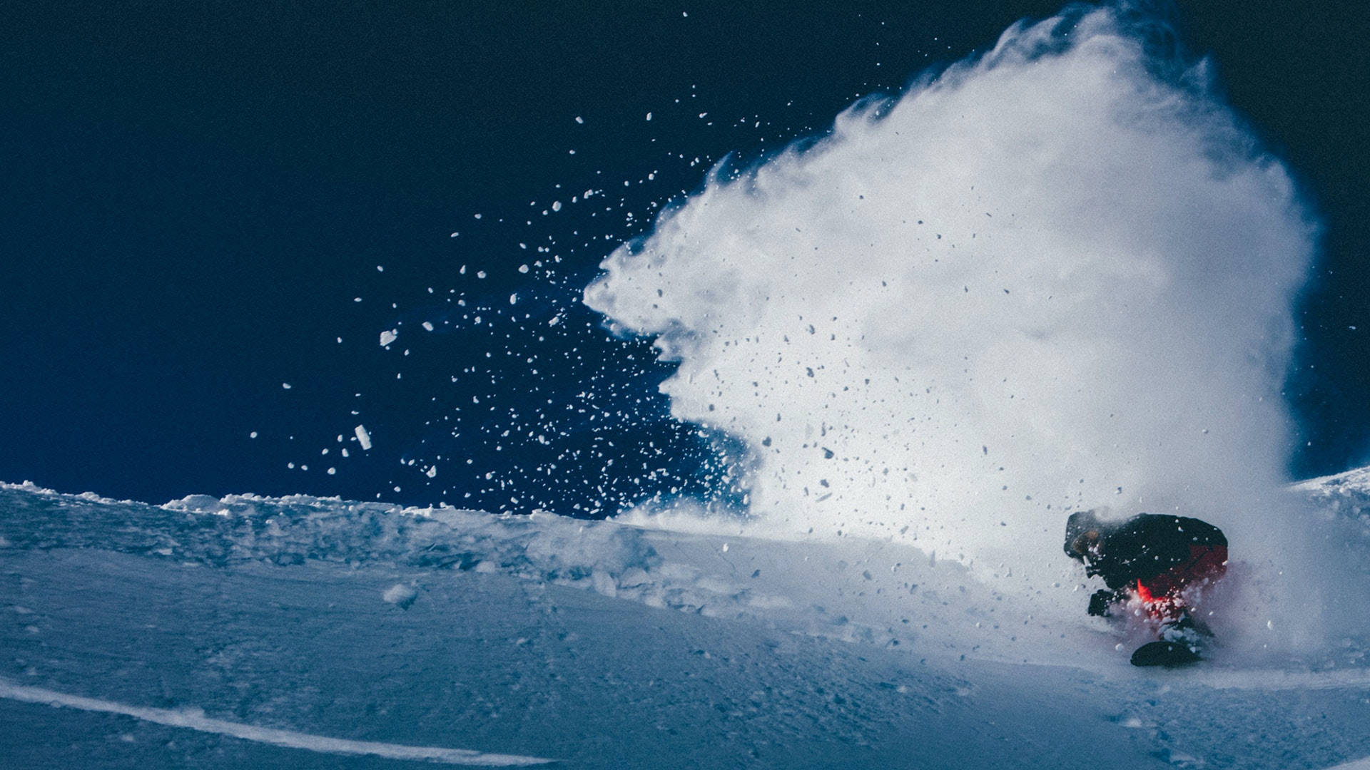 飛雪滑雪 壁紙 — 一名滑雪板運動員在深粉雪中 carving，將大量白色雪花噴向清澈的藍天。