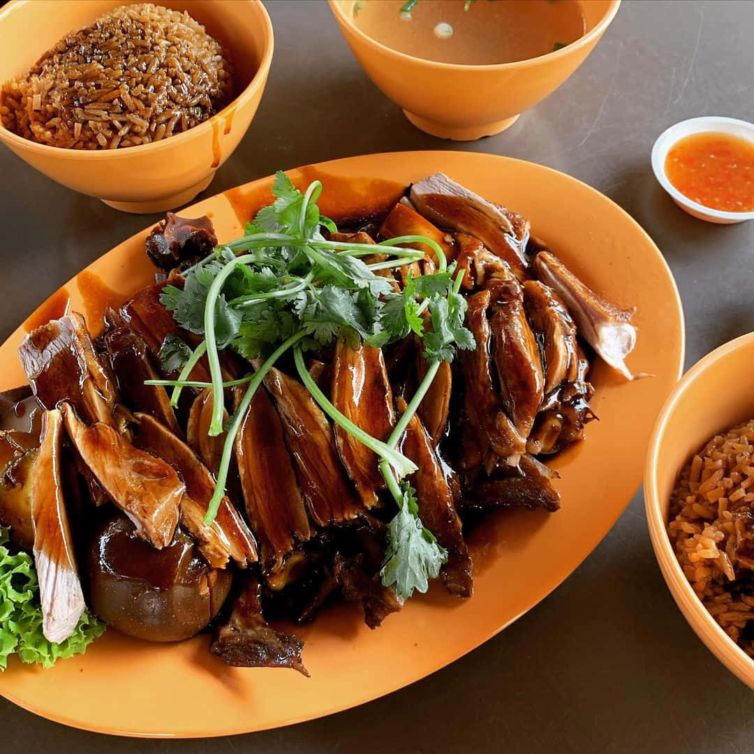 餐廳招牌鴨肉飯，香氣四溢 壁紙 — 閃亮的烤鴨片，飾以芫荽和生菜，放在橙色碟上，配以飯碗和湯碗。