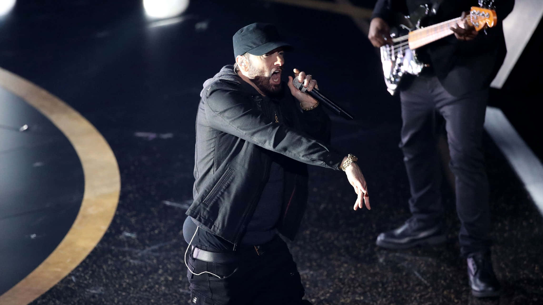 Eminem 桌布 壁紙 — 饒舌歌手Eminem在明亮的聚光燈下，與一位貝斯手一起在黑暗的舞台上熱情表演。