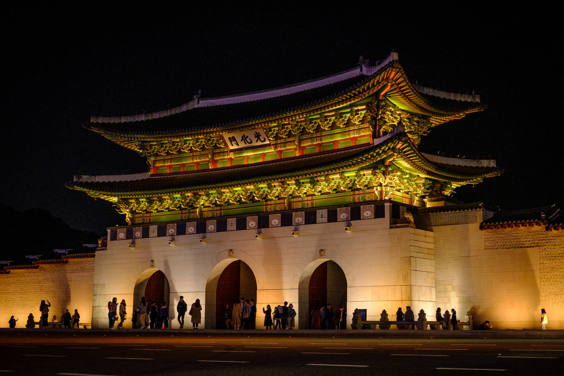 夜間被照亮的傳統韓國大門，人們聚集在周圍。